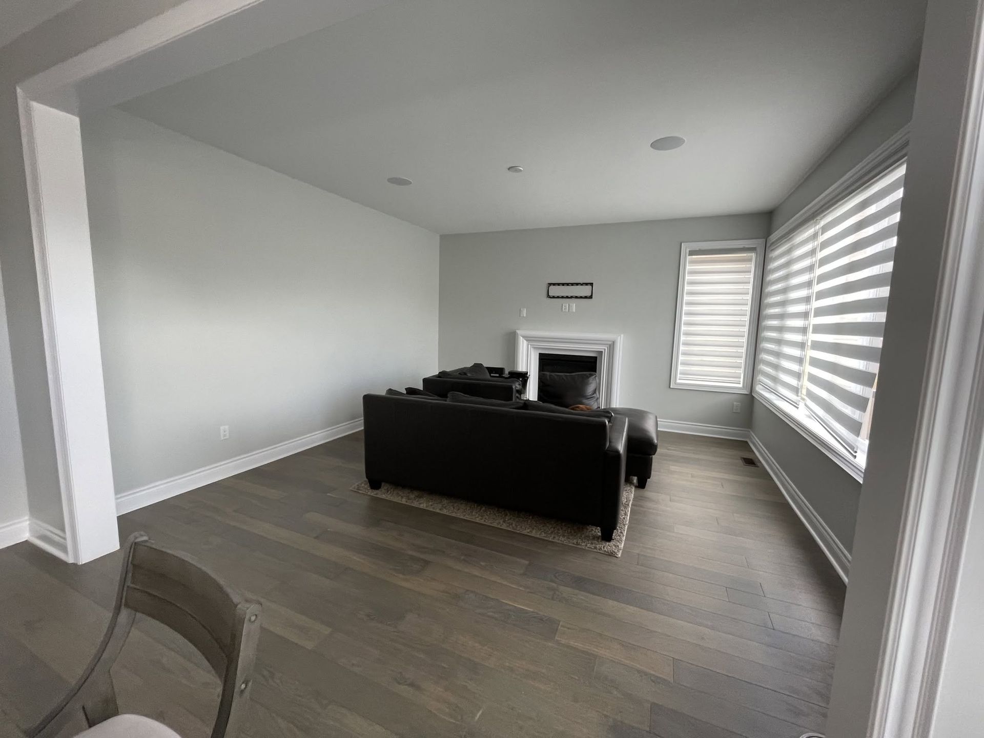 Modern living room with gray walls, dark sofa, fireplace, and large window blinds.