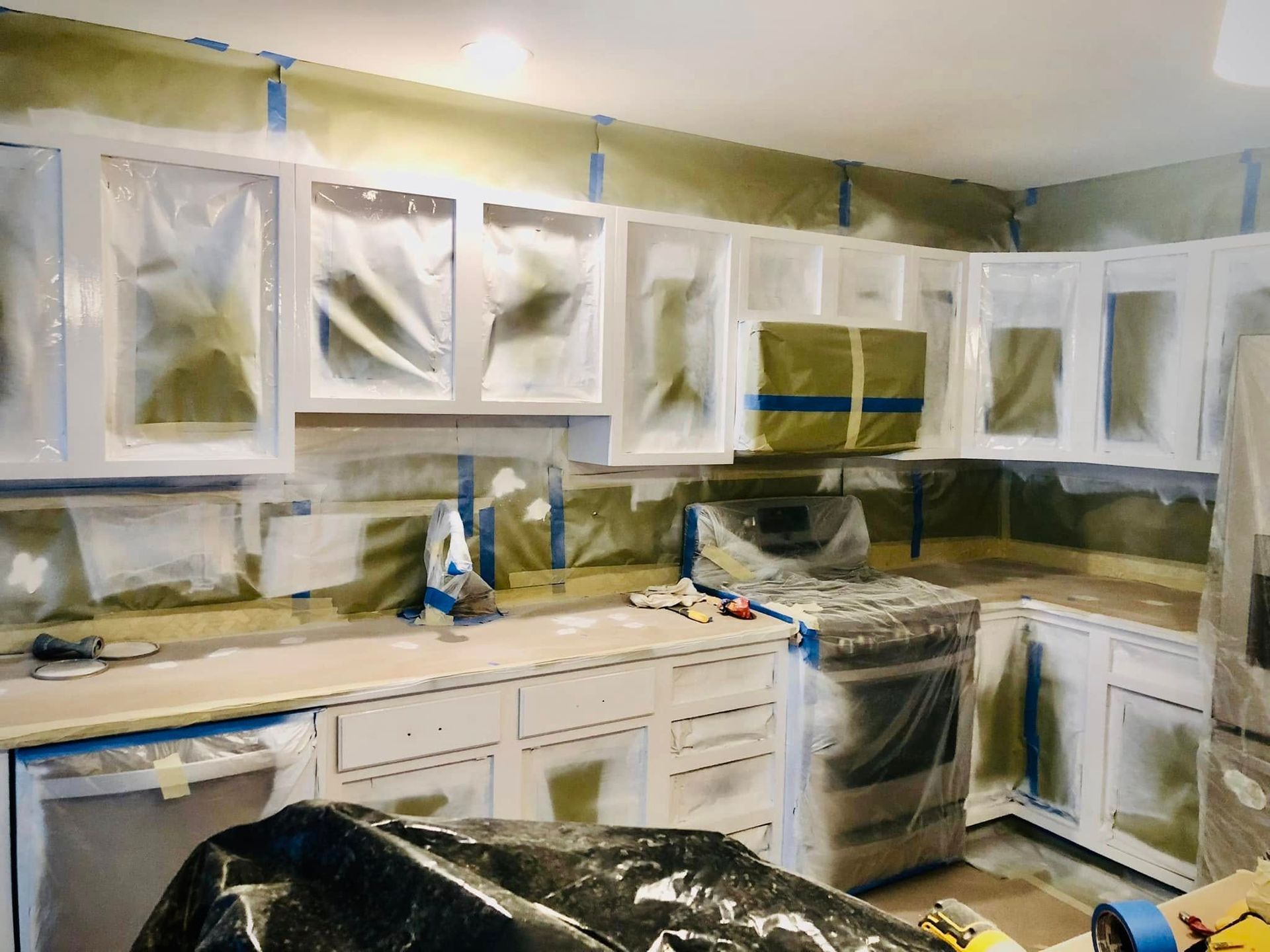 Kitchen cabinets and counters covered in white plastic sheeting during renovation, with a stove and sink visible.