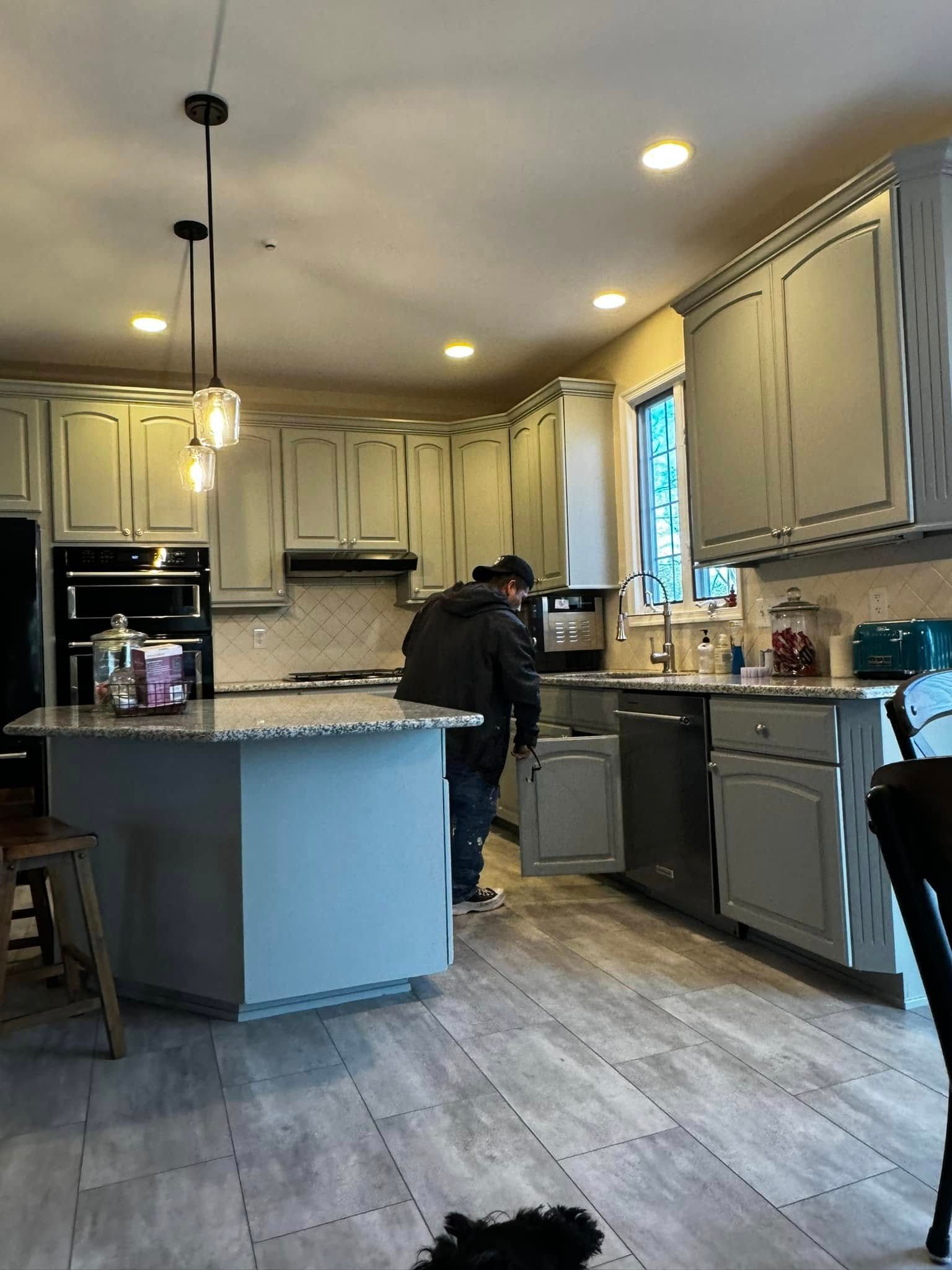 Modern kitchen with gray cabinets, island, and a person standing at the sink.