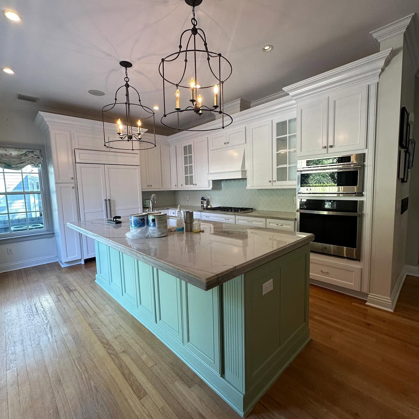 Bright white kitchen with mint-blue island, marble countertops, and hanging chandeliers