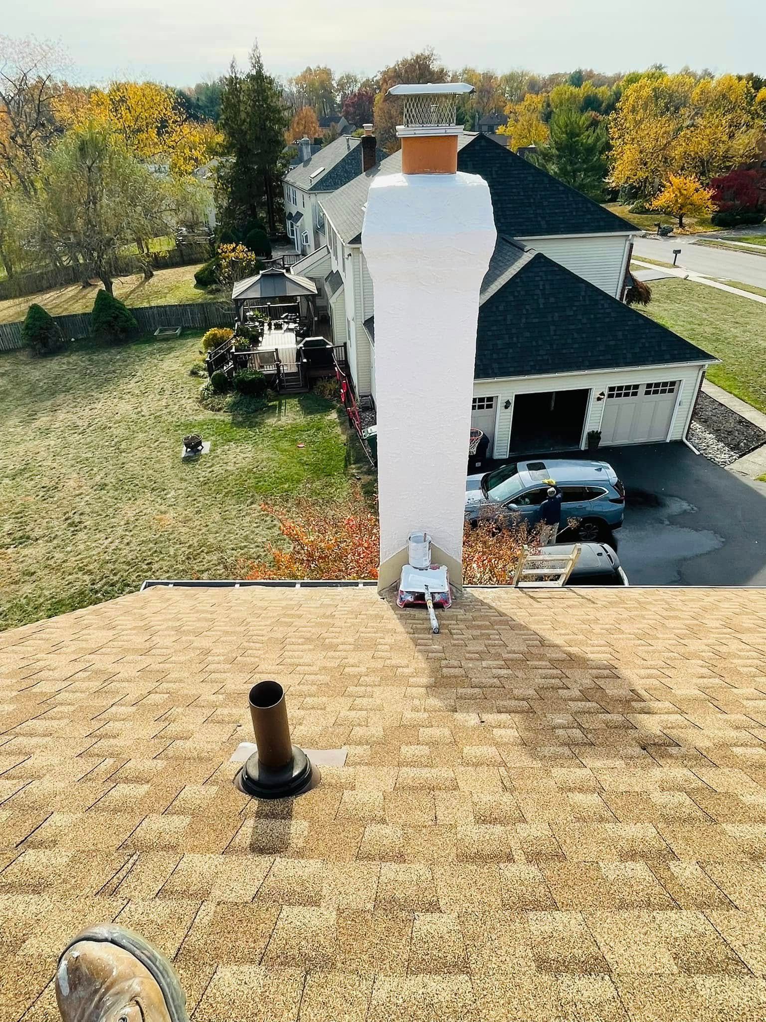 Rooftop view of a house chimney and shingled roof with autumn trees and parked cars below