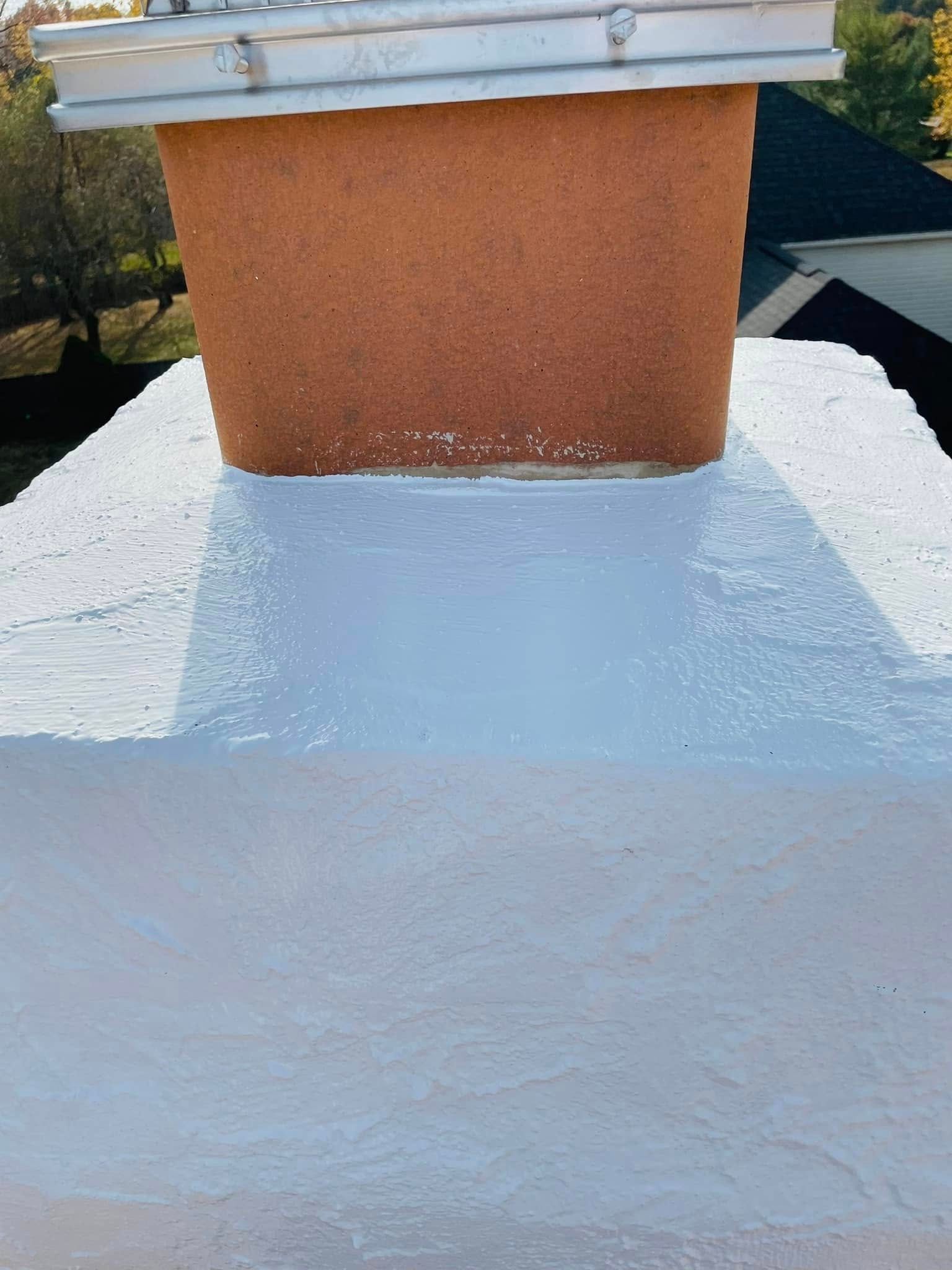 White roof coating around a brick chimney under a metal cap.