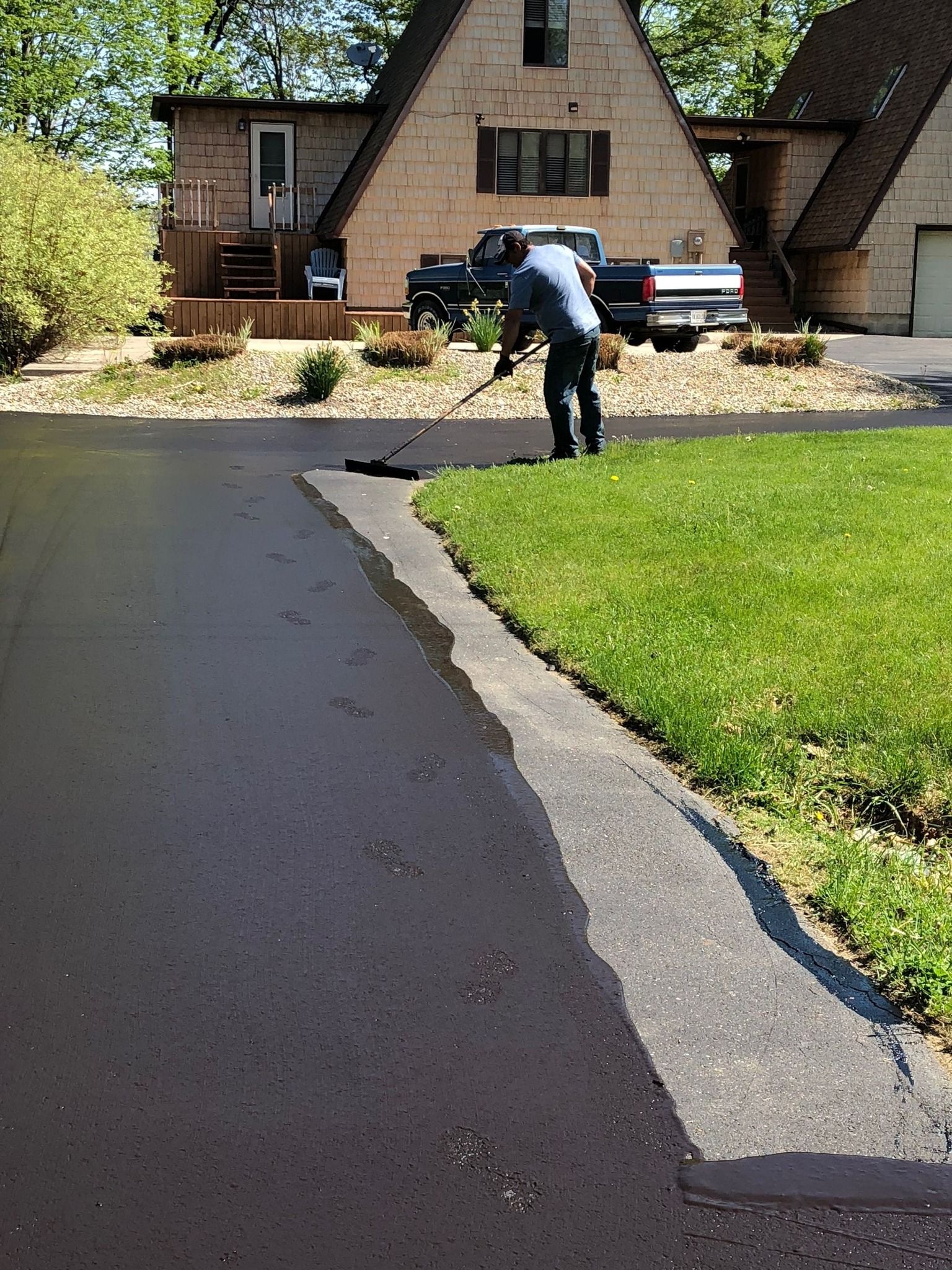 A man is painting a driveway in front of a house