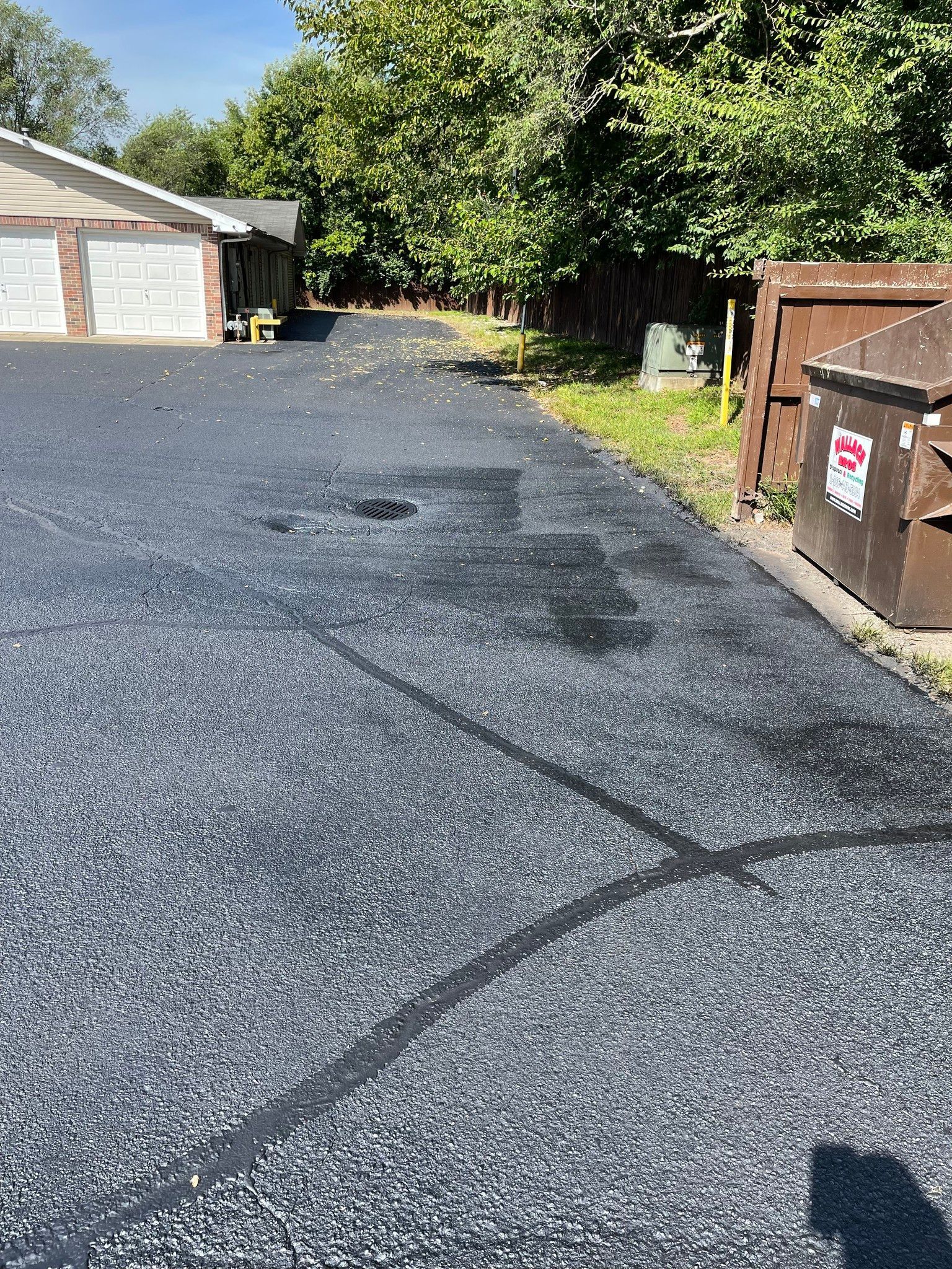 A driveway with a dumpster on the side of it and a house in the background.