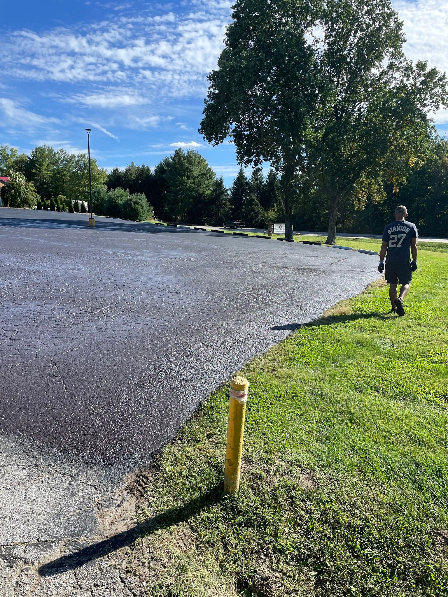 A man is walking down a dirt road next to a grassy field.