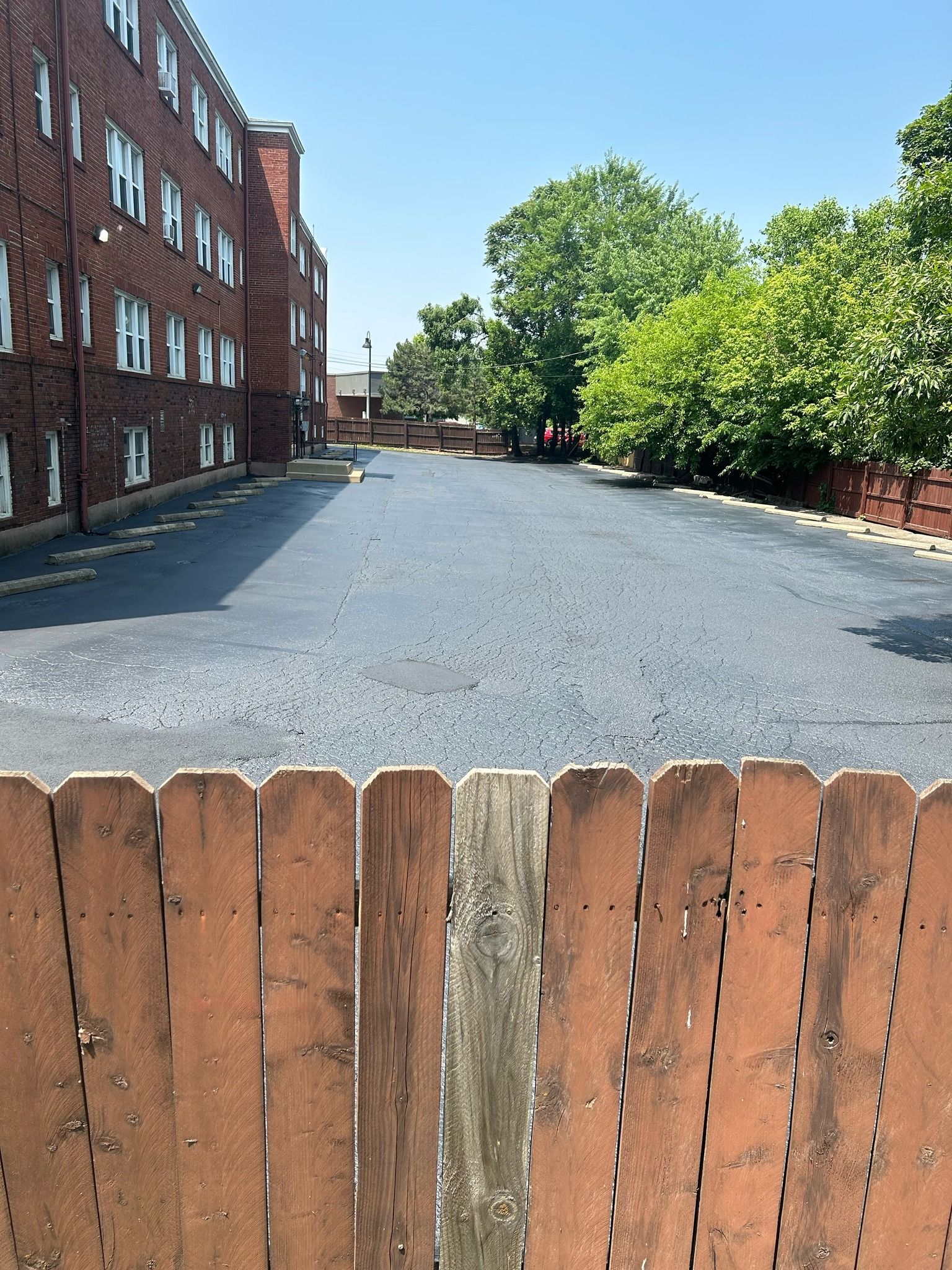 A wooden fence surrounds an empty parking lot in front of a brick building.