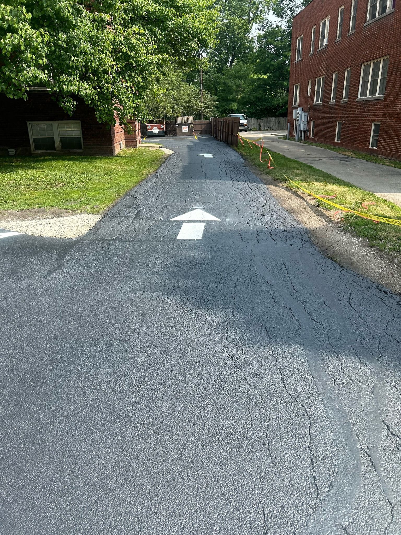 A road with a white arrow pointing to the right and a brick building in the background.