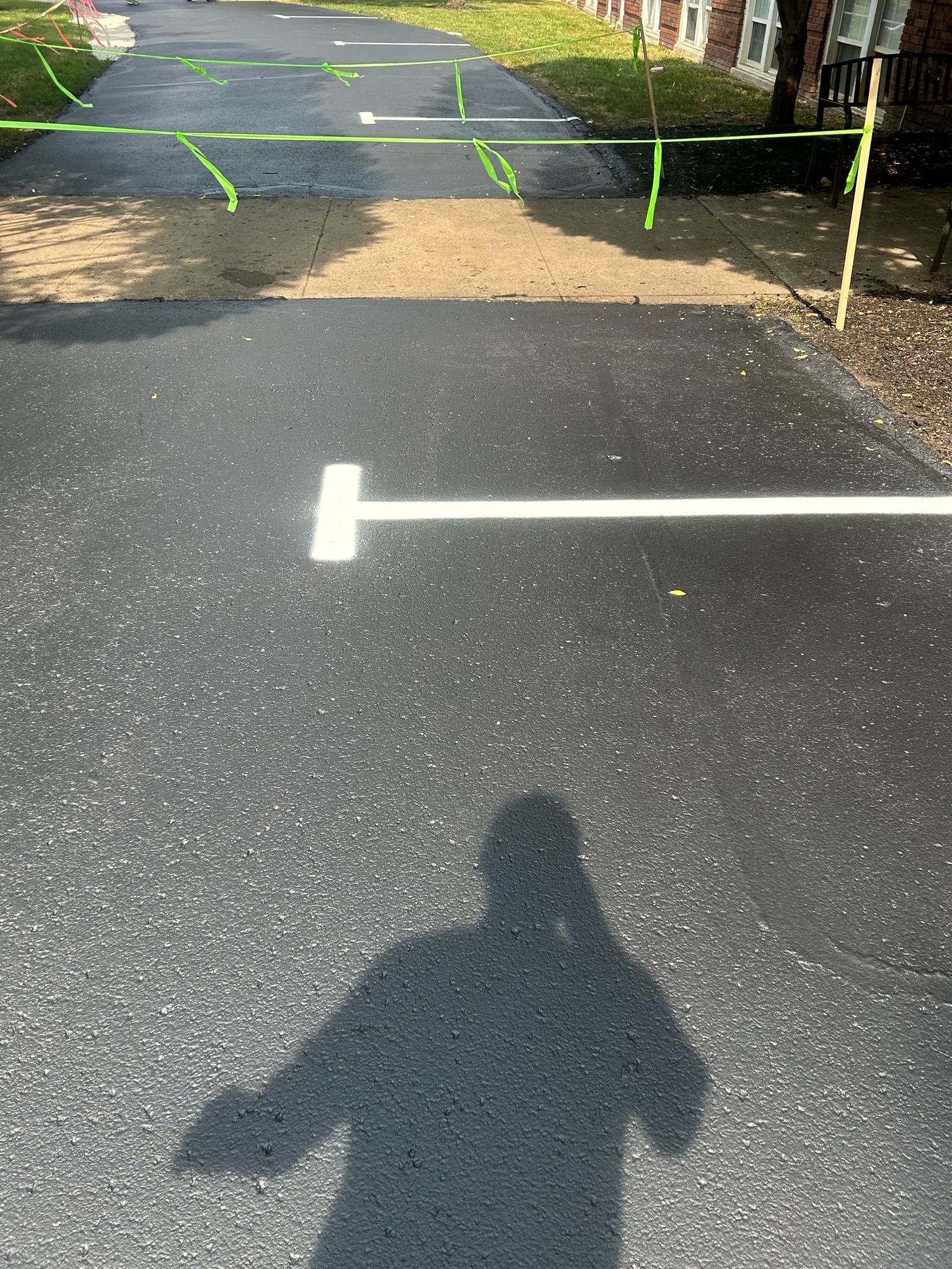 A shadow of a person is cast on the asphalt of a parking lot.