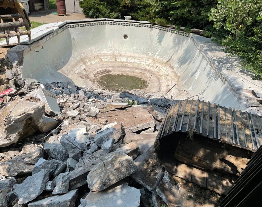 A swimming pool is being demolished by a bulldozer.