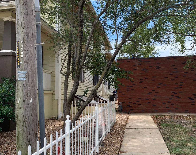A white fence surrounds a sidewalk in front of a brick house.