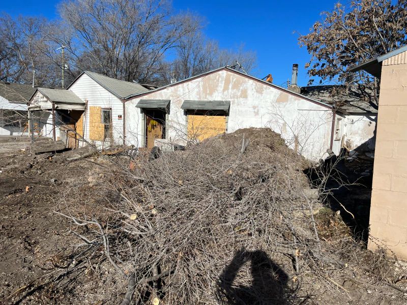 A shadow of a person is cast on a pile of dirt in front of a house.