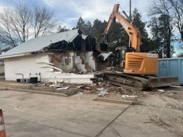 A case excavator is demolishing a building in a parking lot.