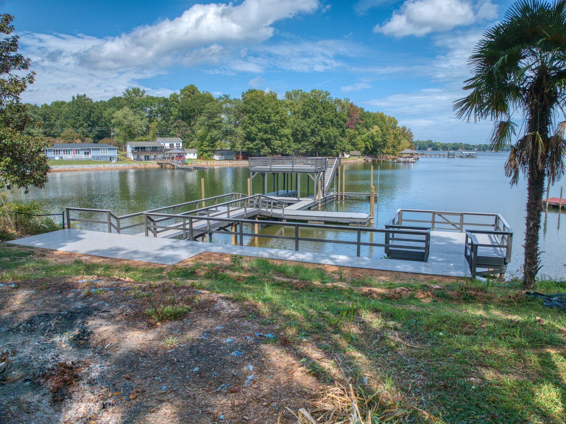 Dock on a lake with a covered boat slip, concrete patio, and trees in the background under a blue sky.