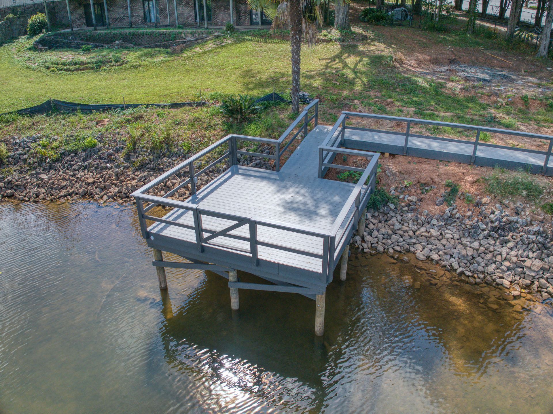 Dock extending from rocky shoreline into water. Grey deck with railings.