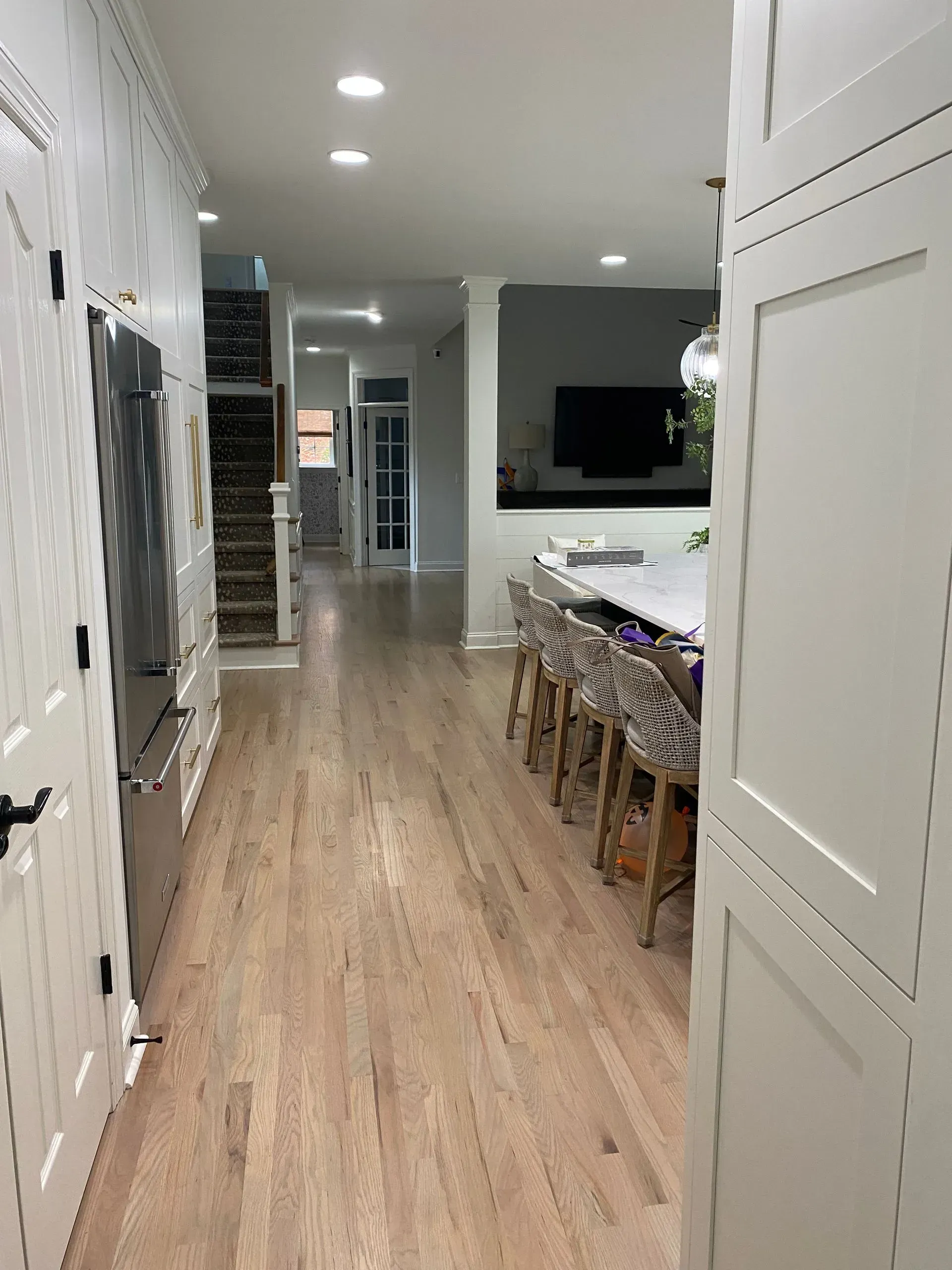 Long, narrow kitchen hallway with white cabinets, light wood floor, and a large kitchen island.