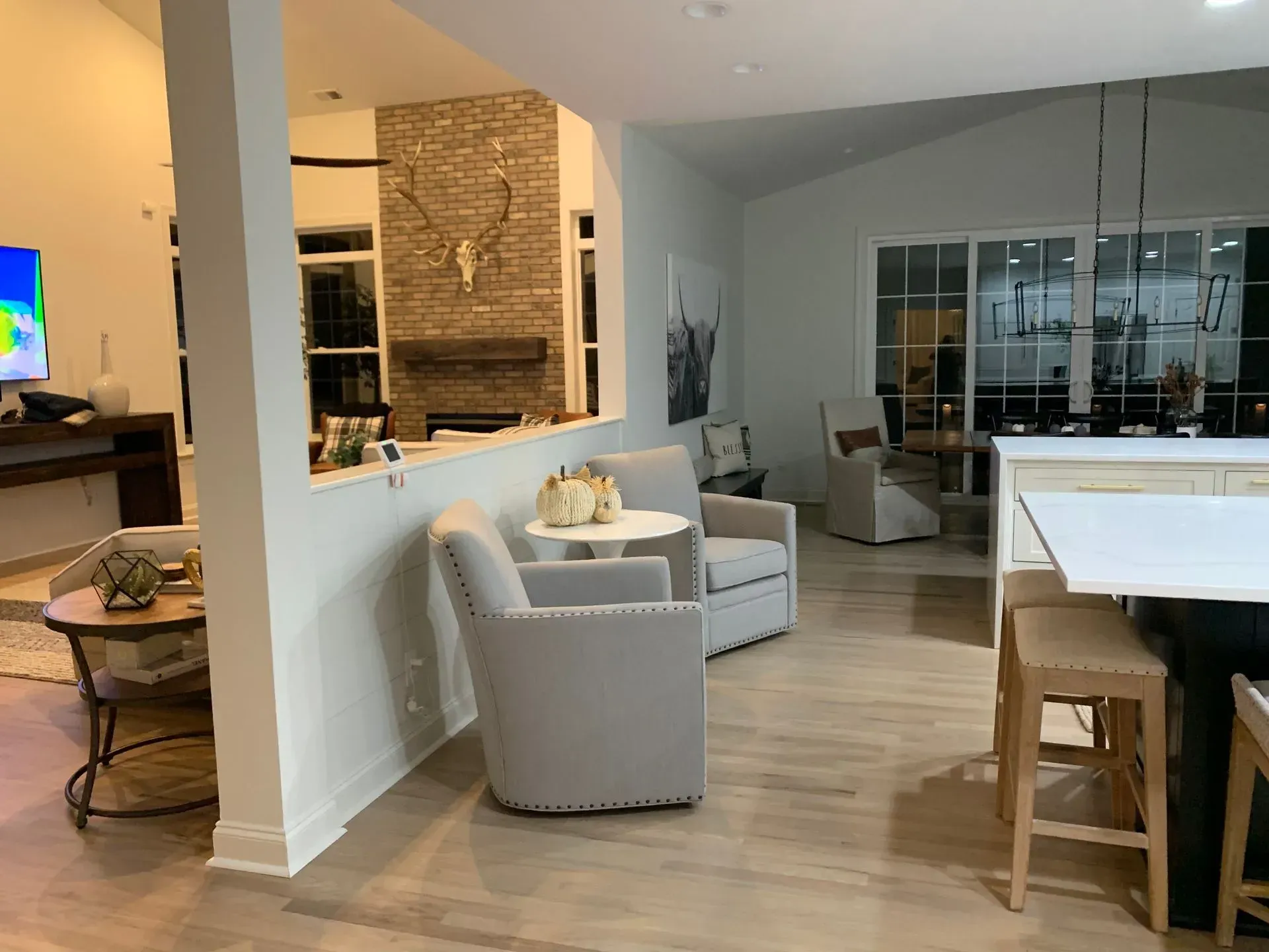 Open-concept living space with seating area, fireplace, and kitchen island. Light walls, wooden floors, and natural light.
