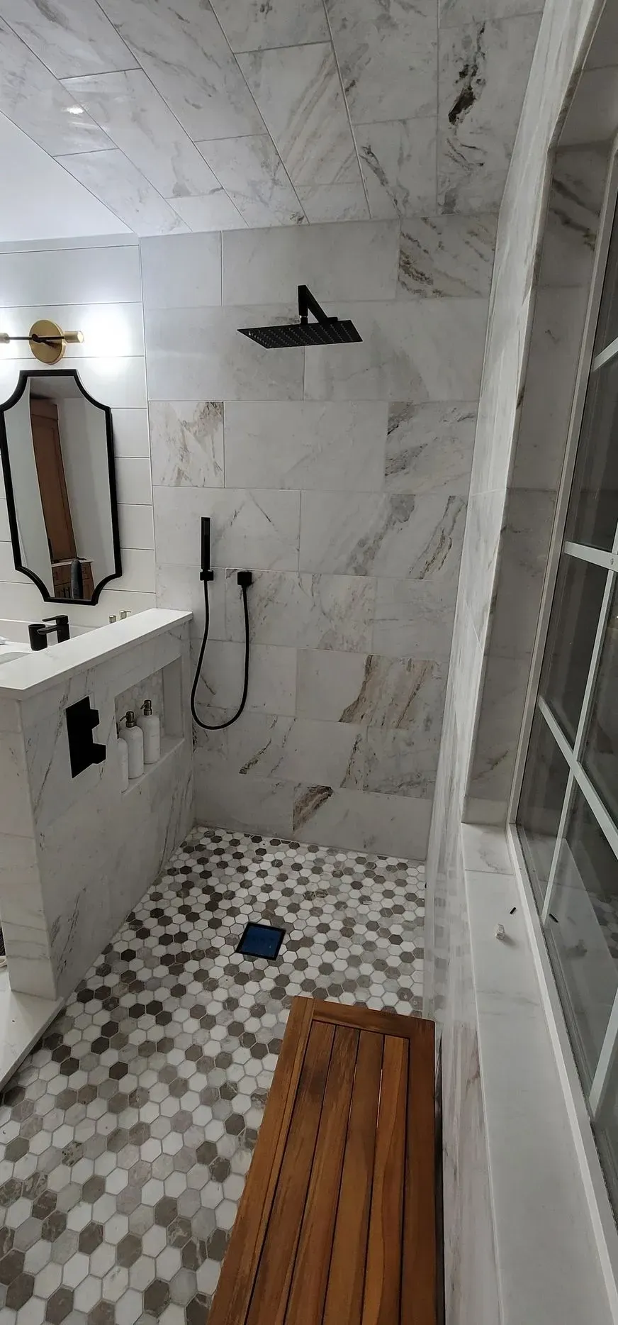 Bathroom with marble tile, black fixtures, and wooden bench.