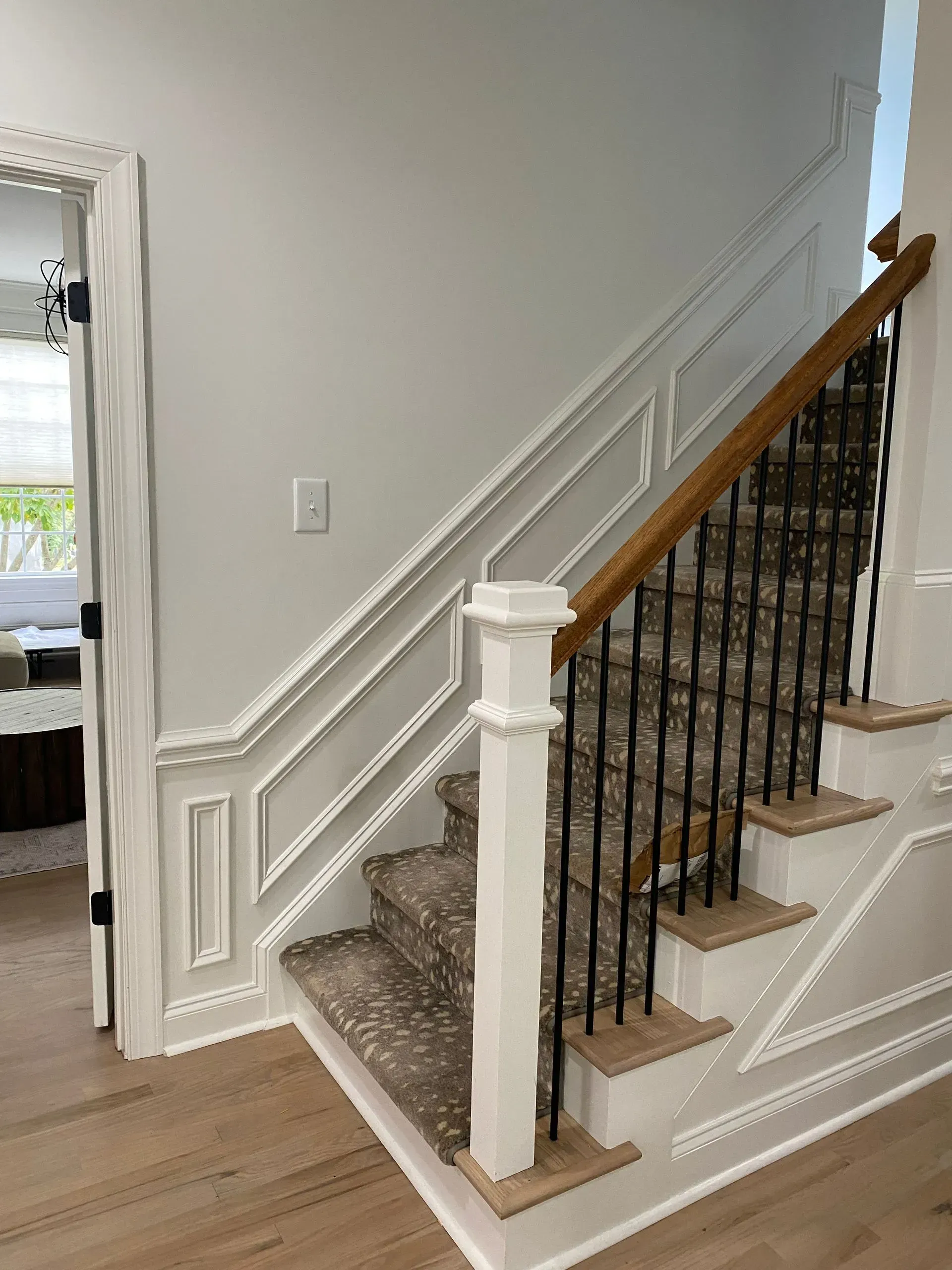 Staircase with white trim, light-colored wooden steps, patterned carpet, and black metal railings against a light gray wall.