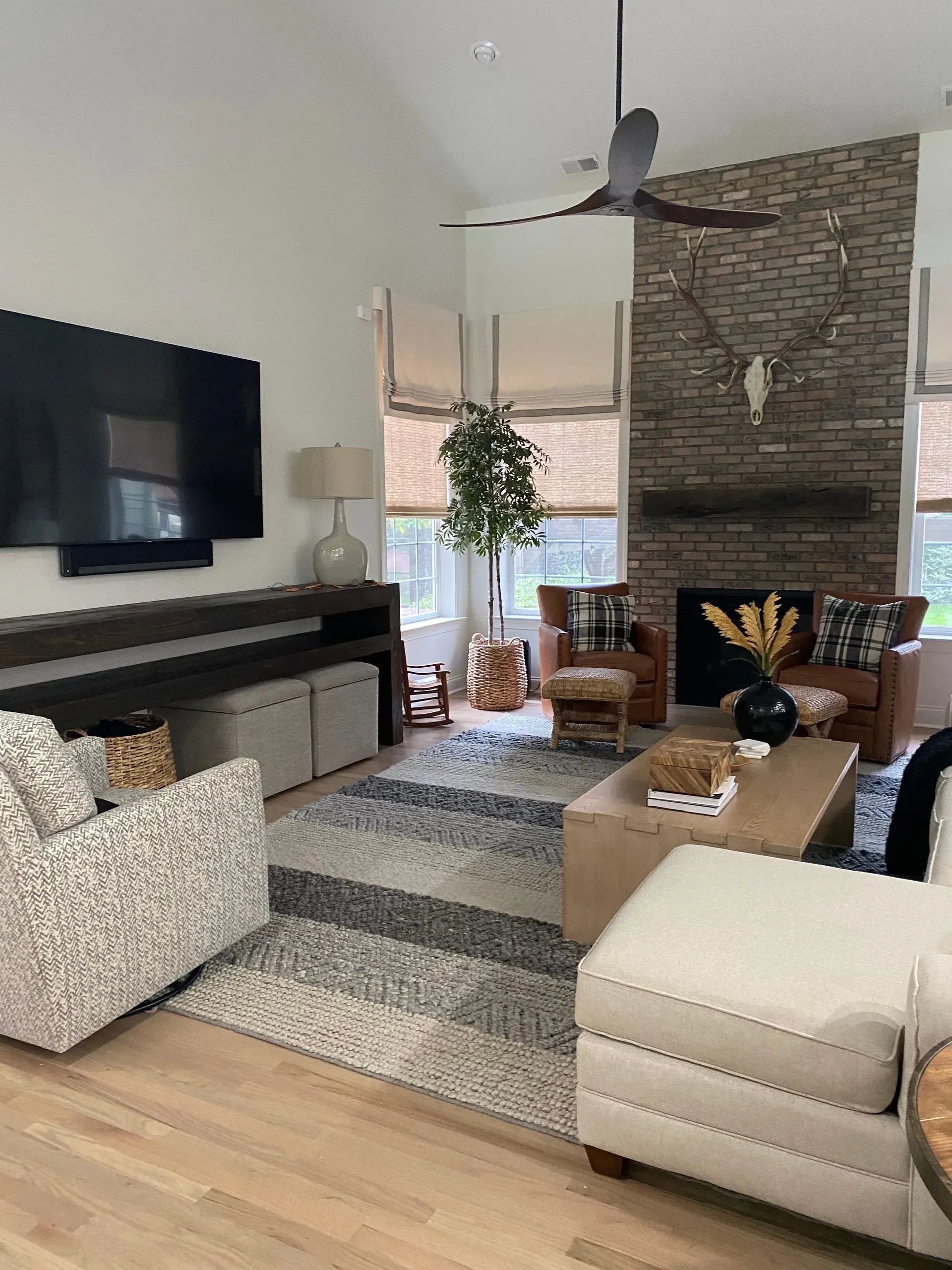 Living room with modern decor: high ceiling, fireplace, large TV, leather furniture, and area rug.