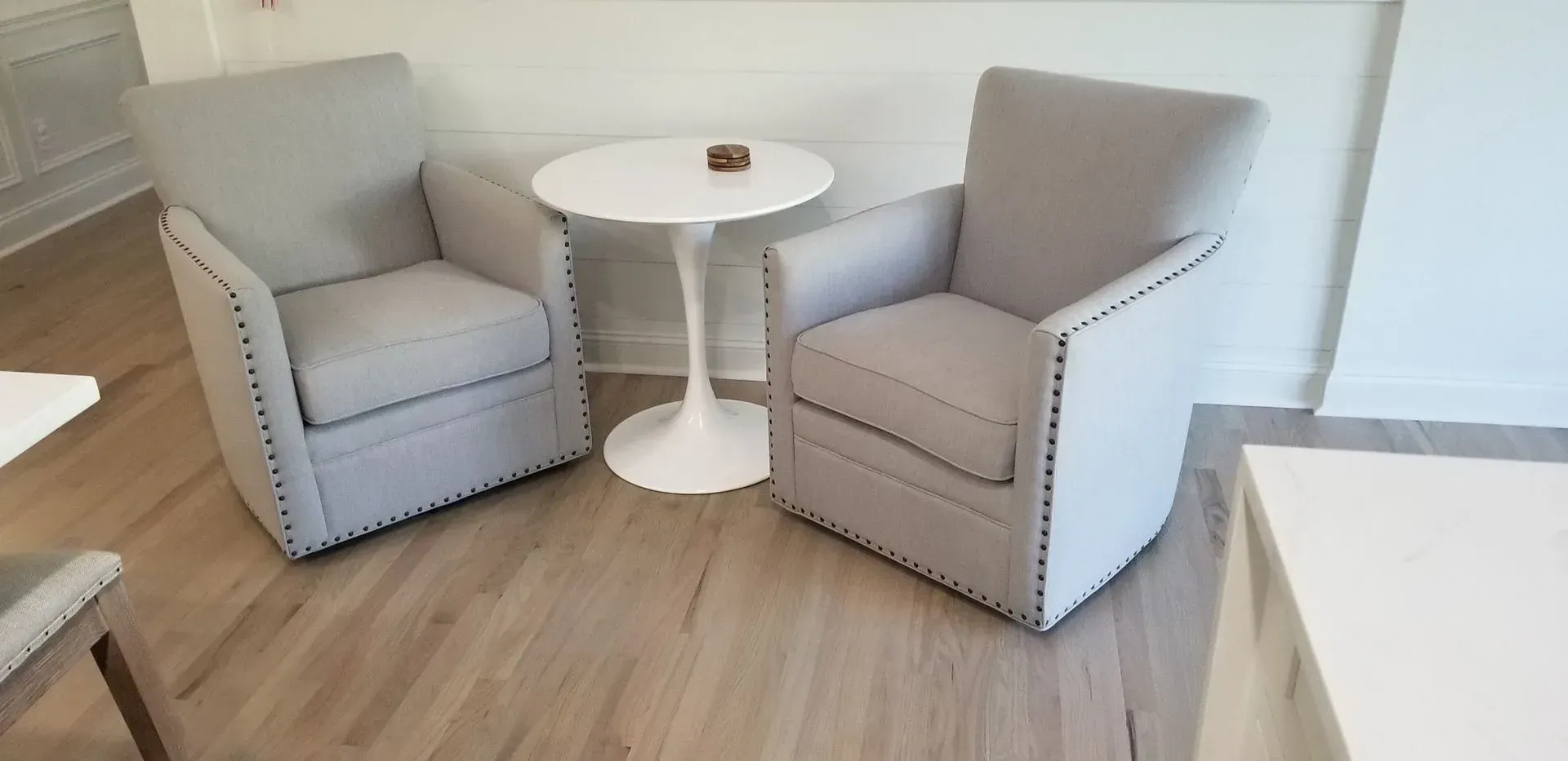 Two gray armchairs and a white side table on a wood floor.