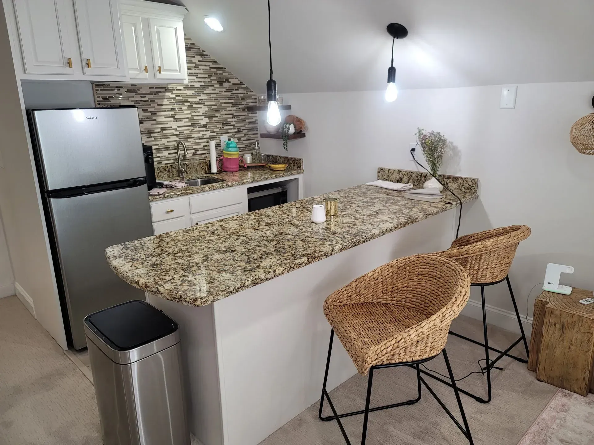 Cozy kitchen with a stainless steel fridge, granite countertop, bar seating, and rattan chairs.