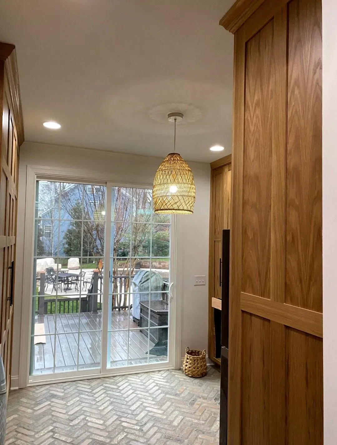 Kitchen interior with hardwood cabinets, a sliding glass door to a deck, and a woven pendant light.