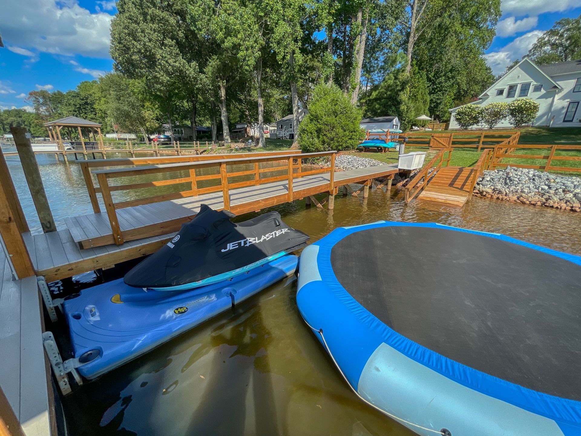 Wooden dock with watercraft alongside, blue jet ski and inflatable paddle board.