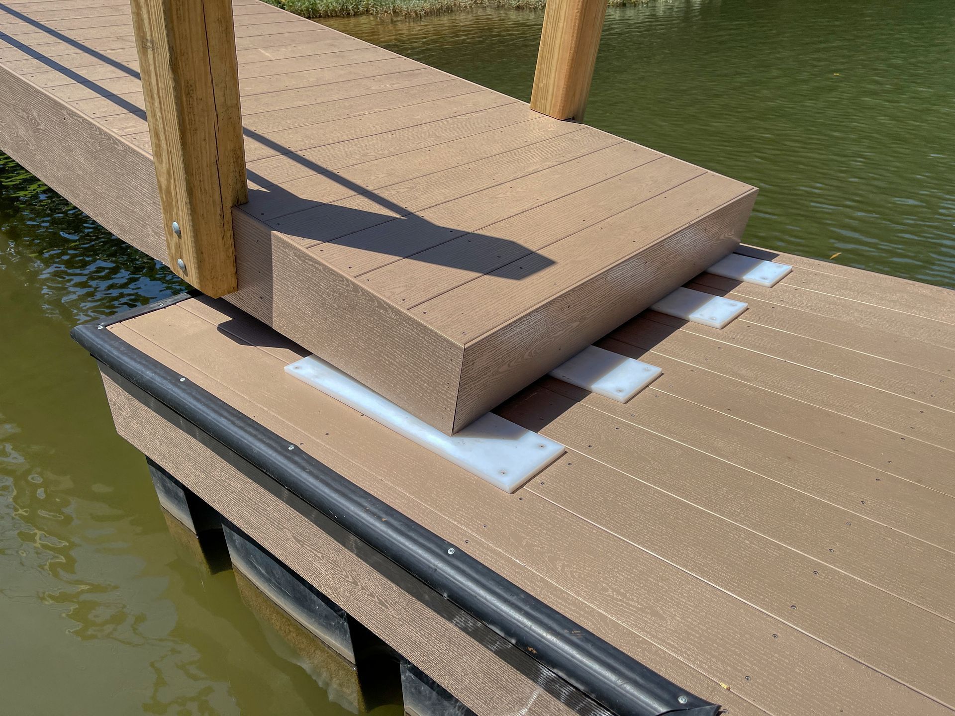 A composite boardwalk extends over water, connected by white pads and wooden supports.