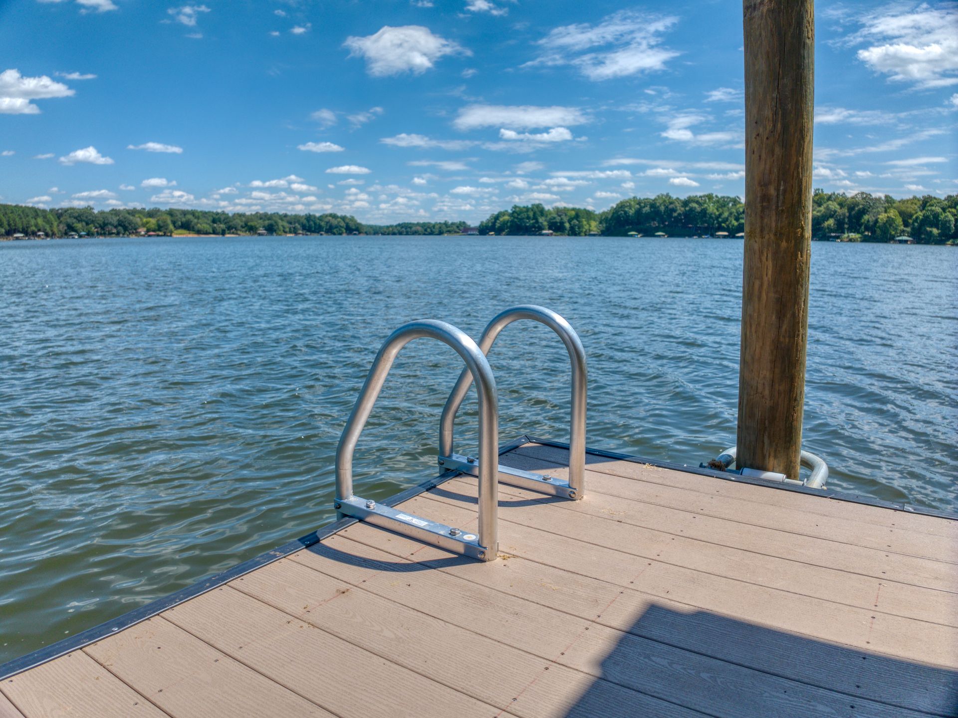 Dock with metal ladder extending into a calm lake, under a blue sky with clouds.