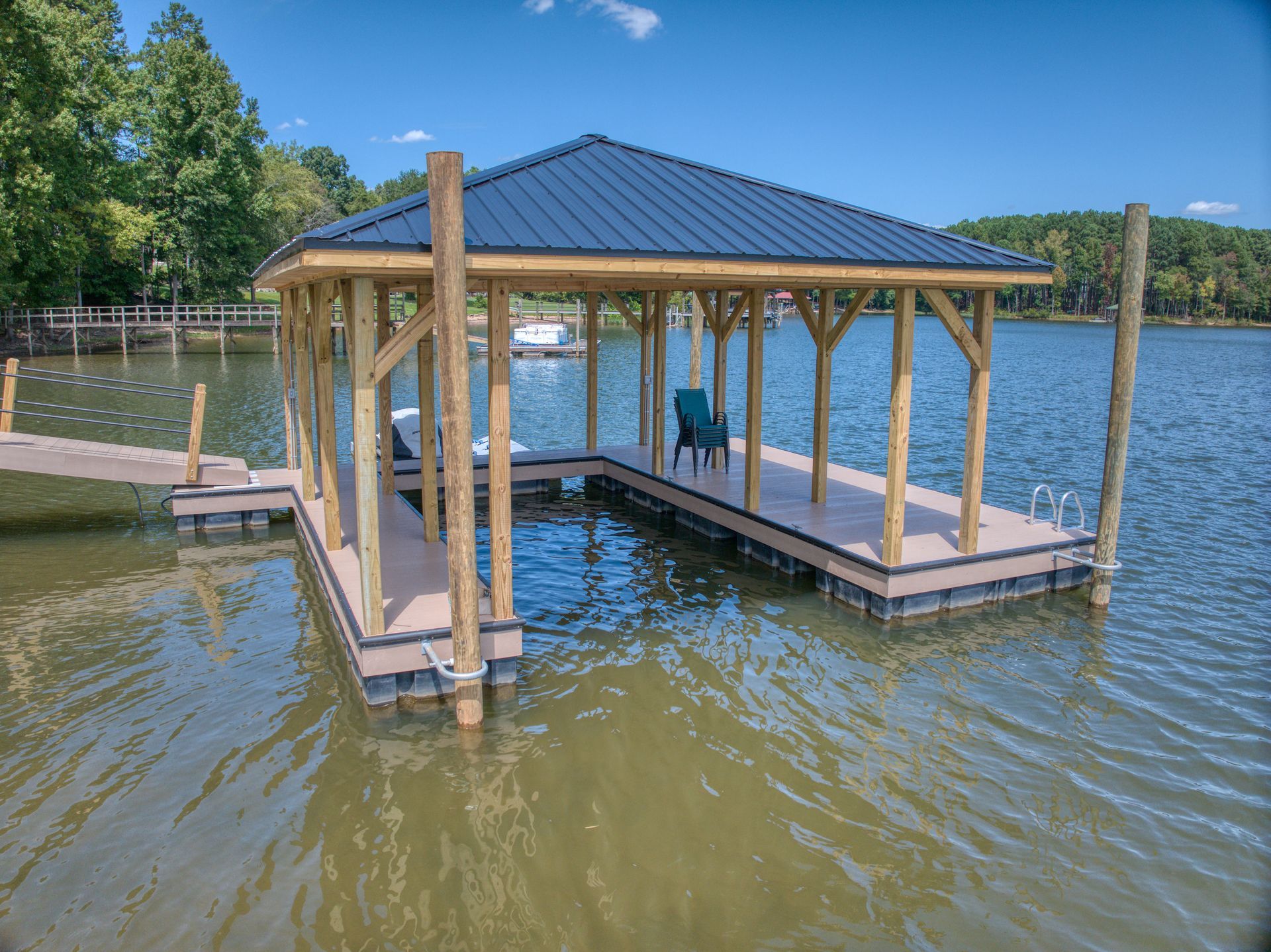 Covered dock on a lake with a blue roof, wood beams, and a chair.