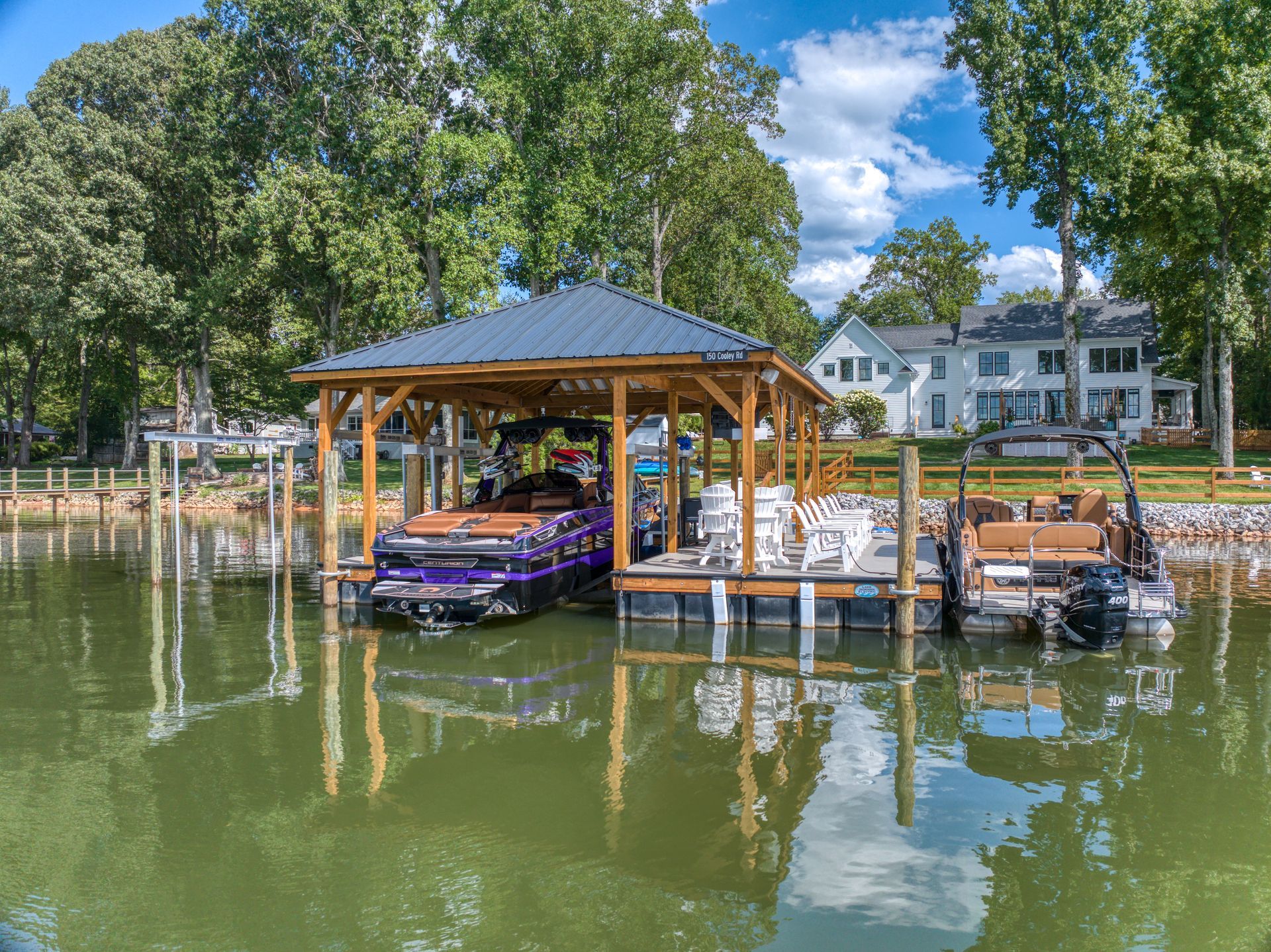 Boathouse with two boats docked on a lake, featuring purple and brown boats, and houses in the background.