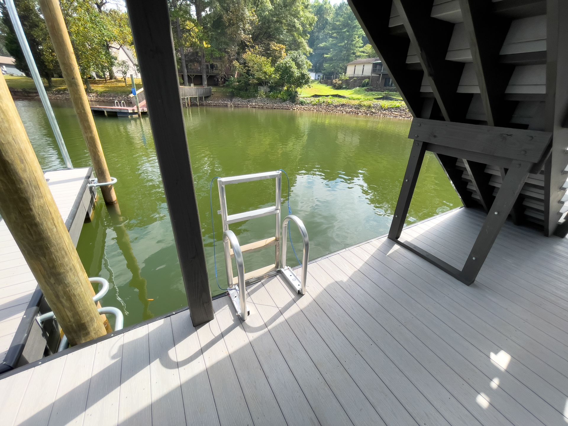 Dock with water ladder, gray deck, lake in background, and wooden support beams.