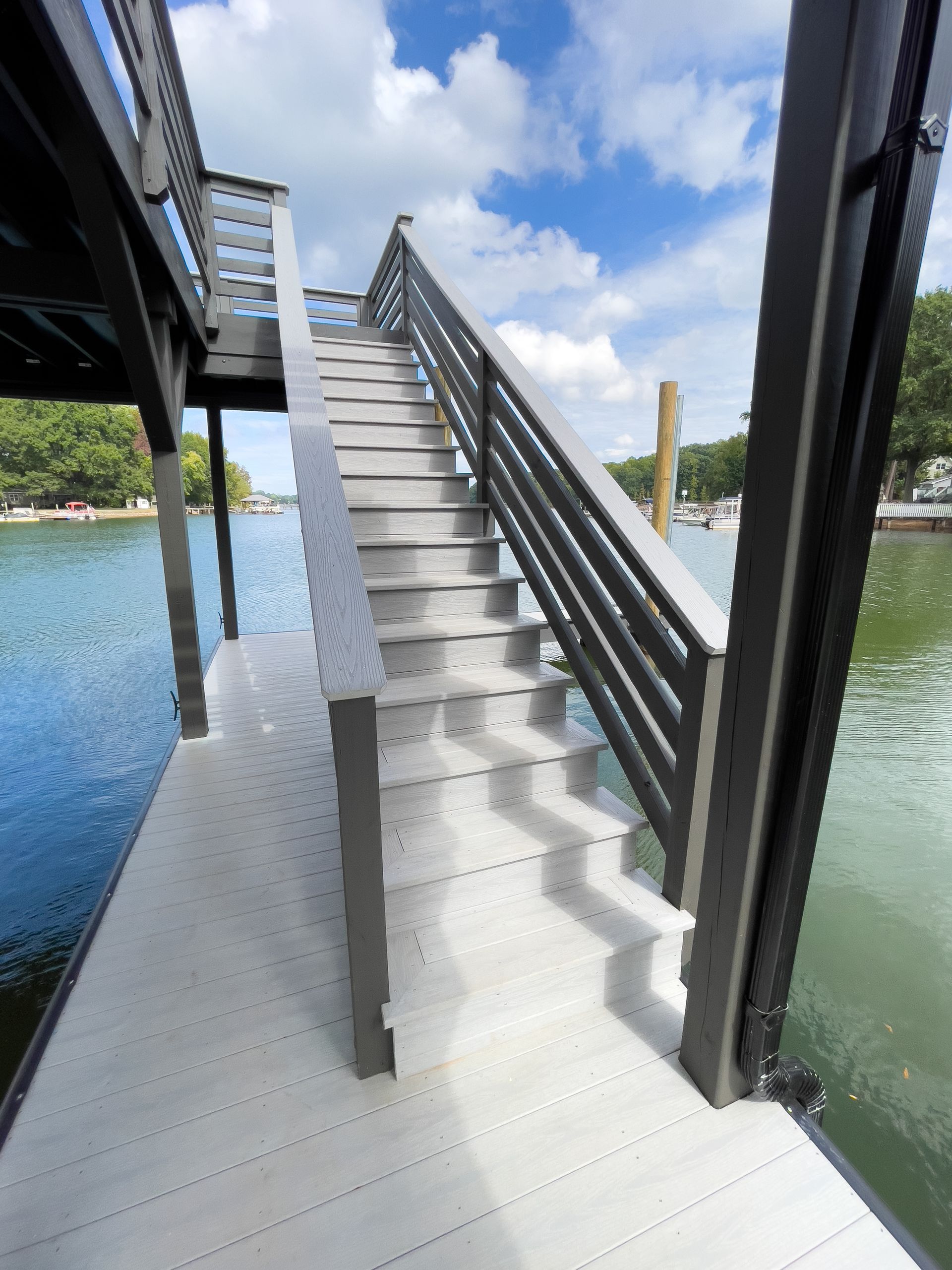 Gray stairs lead up from a dock to a covered structure over water, under a partly cloudy sky.