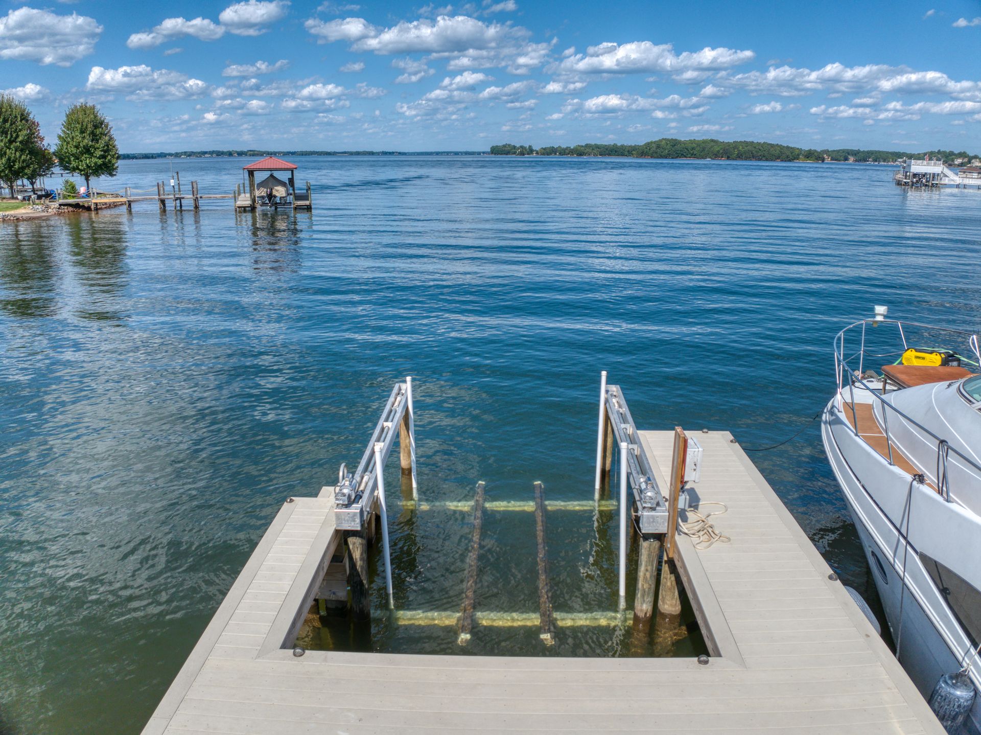 Dock with boat lift, boats on lake under sunny sky.