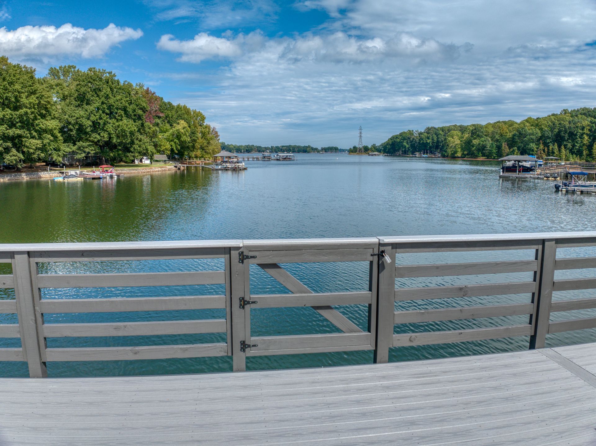 View of a lake from a bridge with a wooden gate, flanked by trees and boats under a cloudy sky.