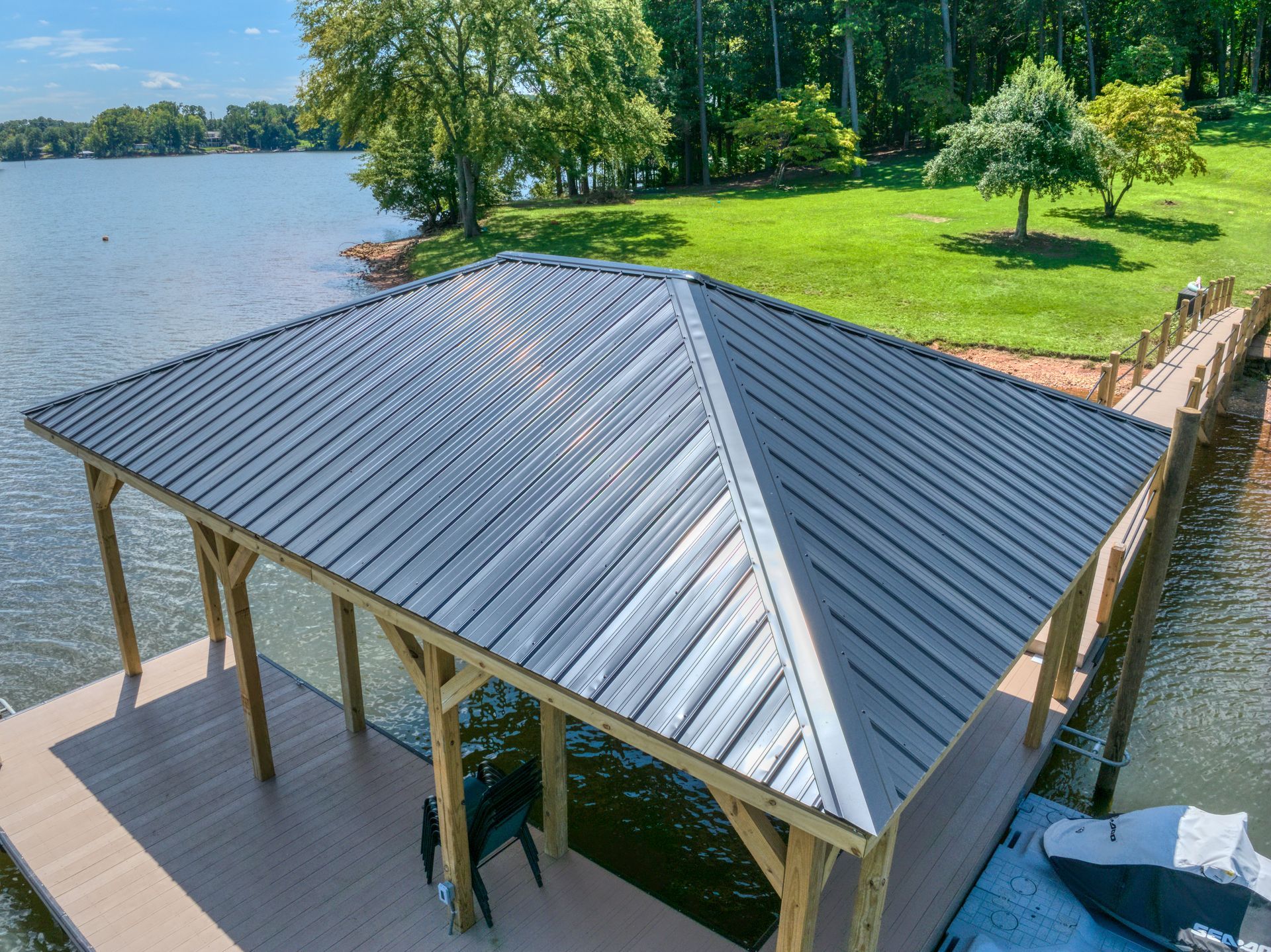 A covered dock with a metal roof on a lake. Wooden posts support the roof.
