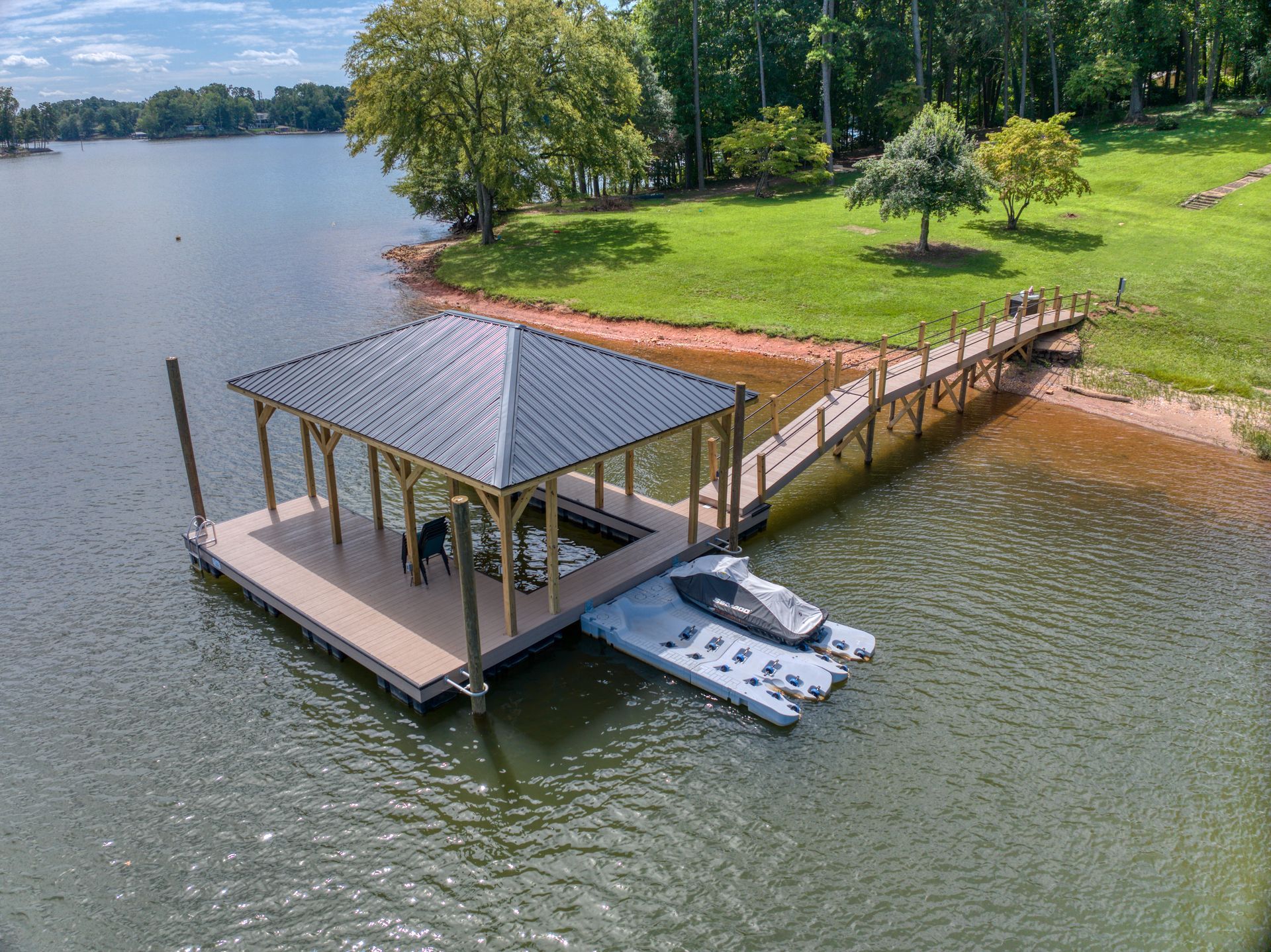 Dock with a boat, roof, and walkway on a lake. Green grass and trees are in the background.