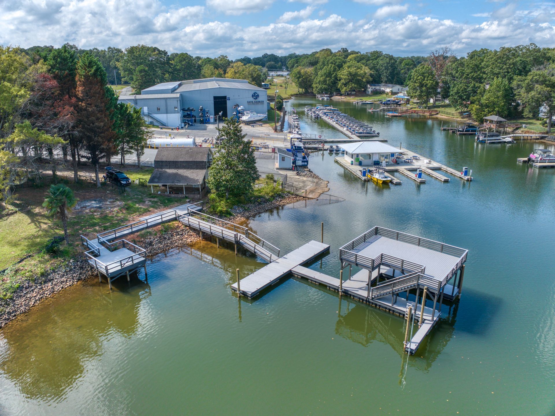 Boats docked at a marina on a lake, with buildings and trees in the background under a blue sky.