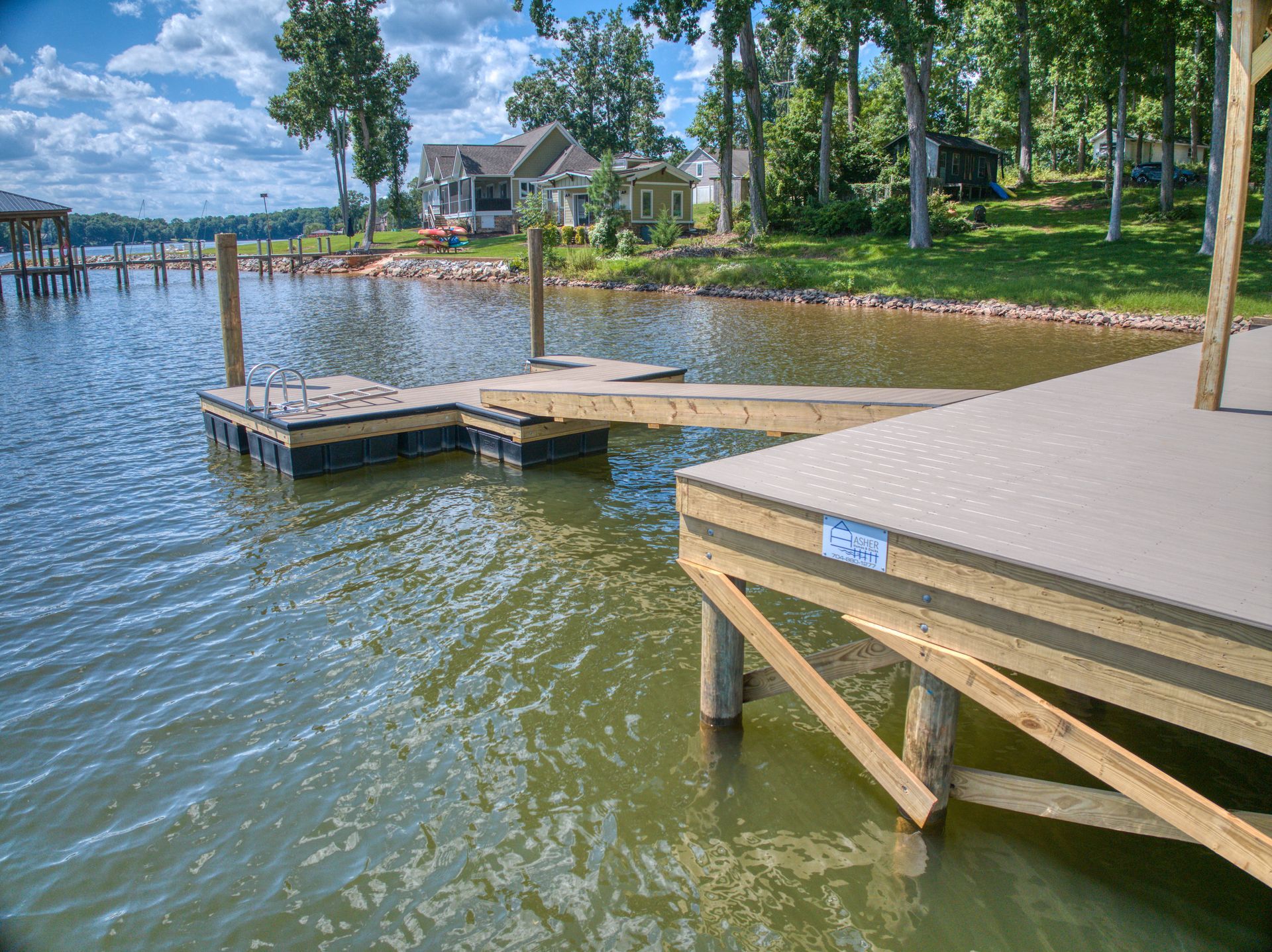 Dock extends into water, with a house and trees in the background under a blue sky.