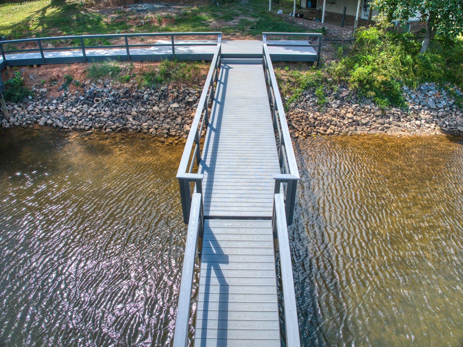 Wooden dock extending into water, with railings on either side. Sunlight reflects on the water's surface.