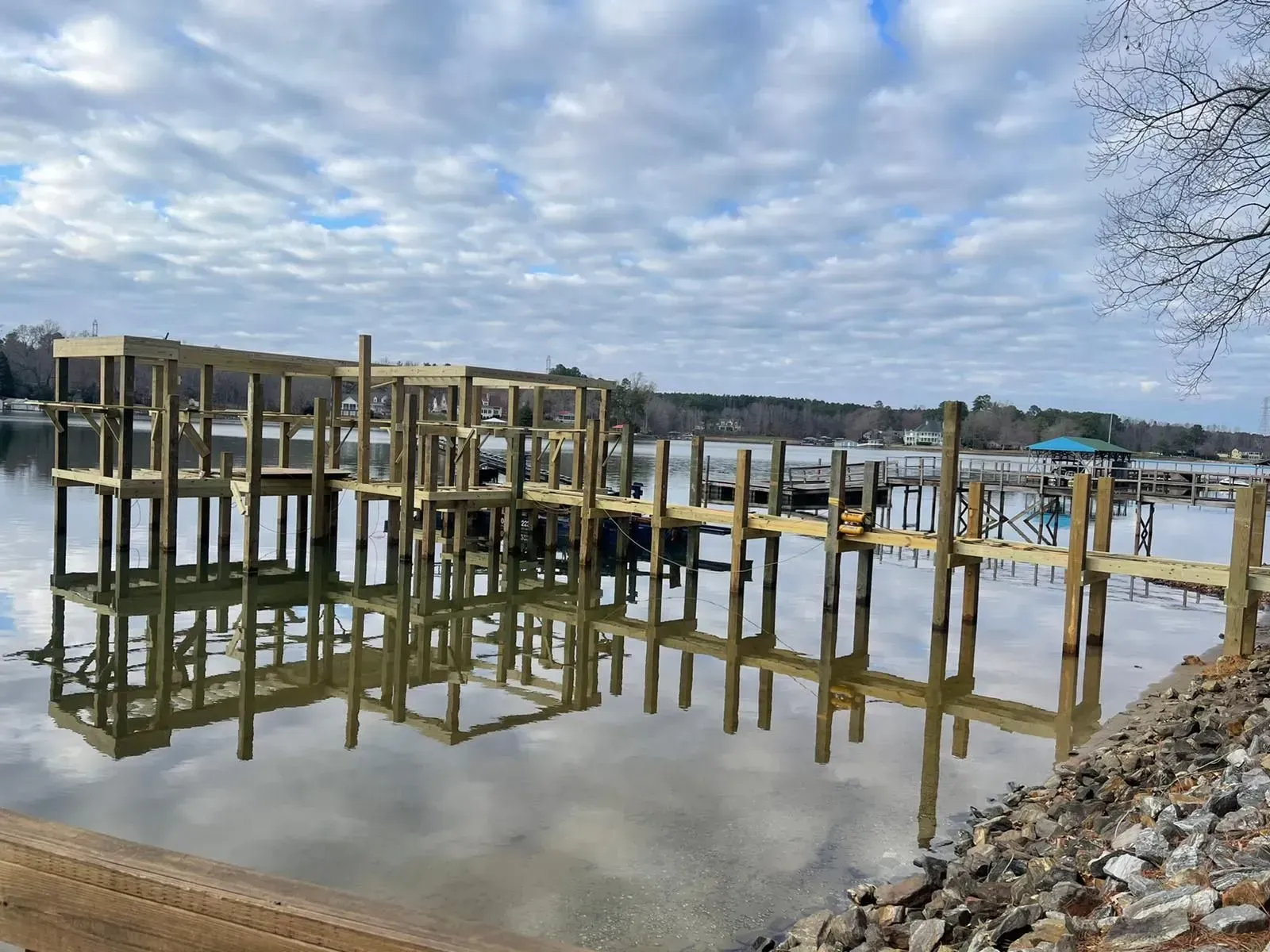 New wooden dock under construction on a calm lake, reflecting the cloudy sky.