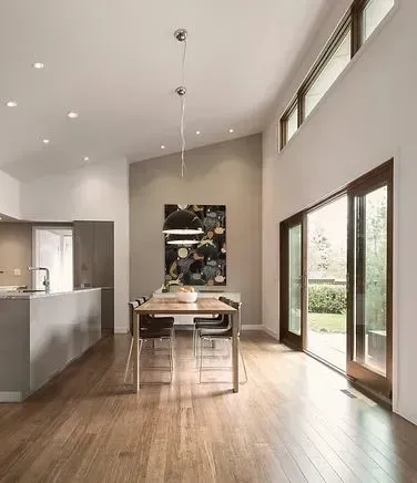 Open-concept kitchen/dining area with wooden floors, neutral walls, modern art, and large glass doors to the backyard.