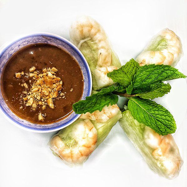 A bowl of dipping sauce next to some shrimp rolls