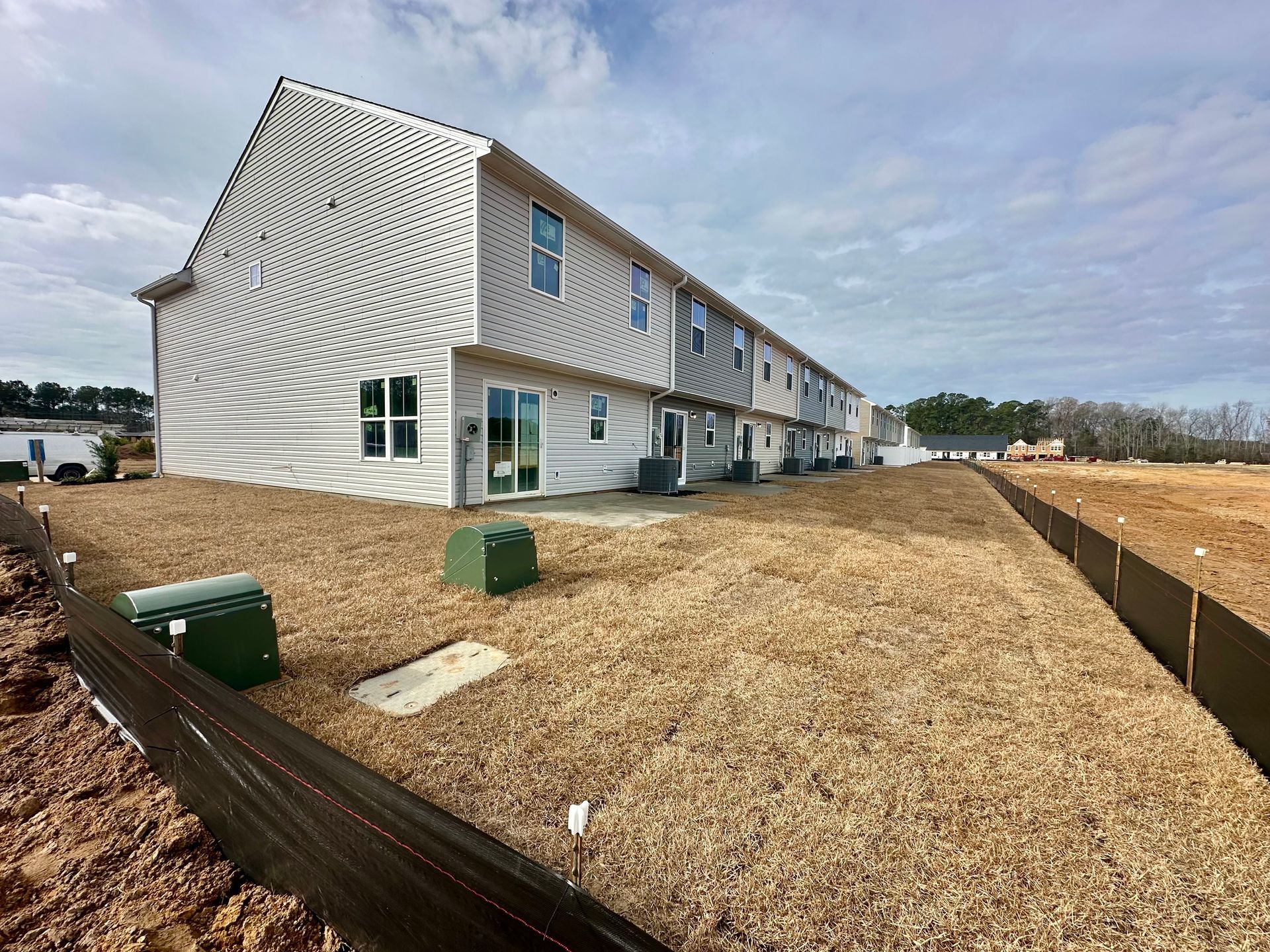 Back view of newly constructed townhomes with beige siding, on a wood chip covered lot.