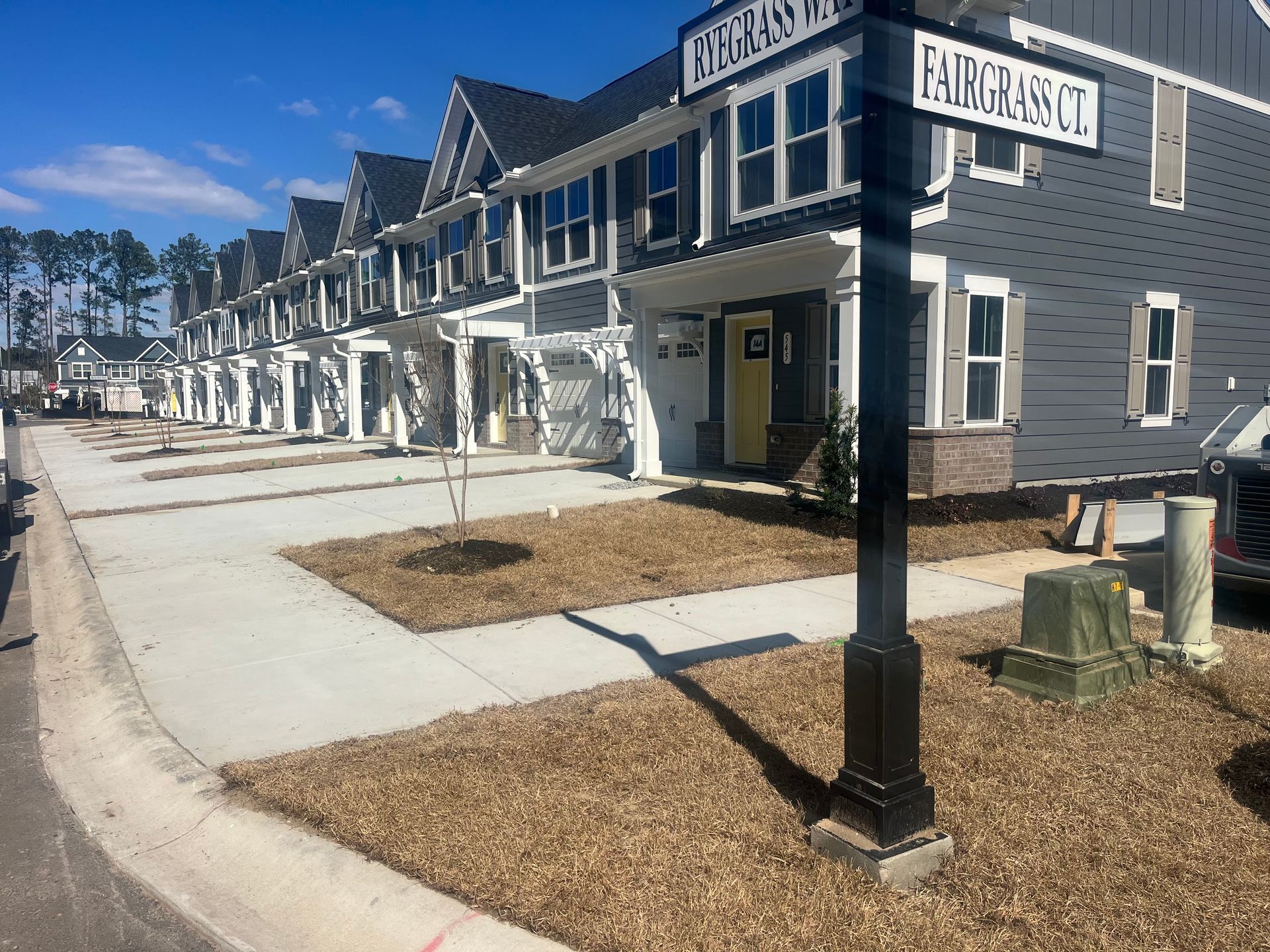 Townhouses with dark gray siding, white trim, and a street sign on a sunny day.