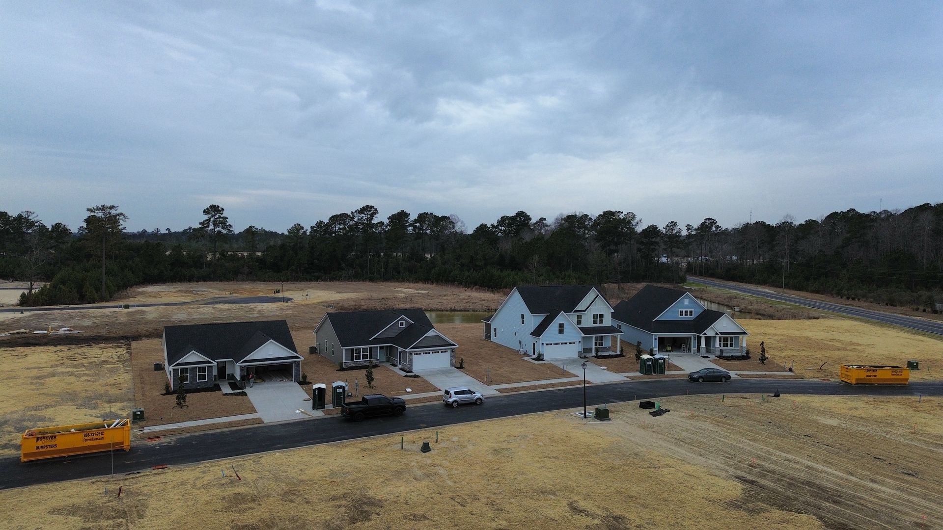 New houses under construction on a grassy lot. Several vehicles are present under a cloudy sky.