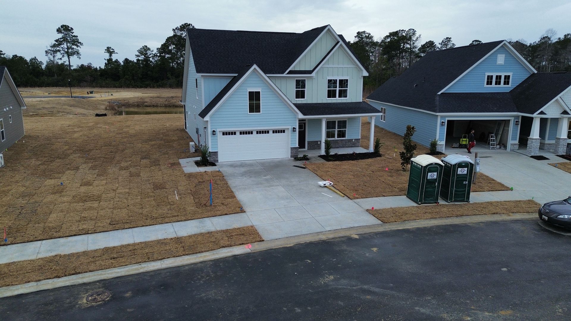 Blue house with white garage and driveway in a new development, with two porta-potties in the yard.