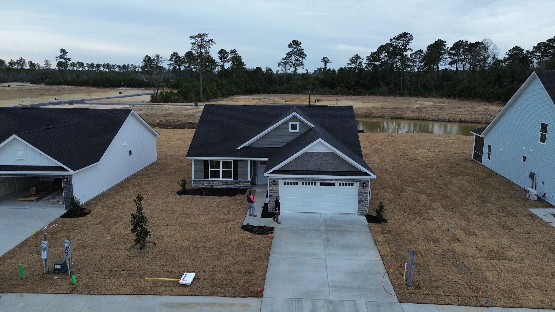 A gray house with a white garage door, surrounded by brown grass and other houses.