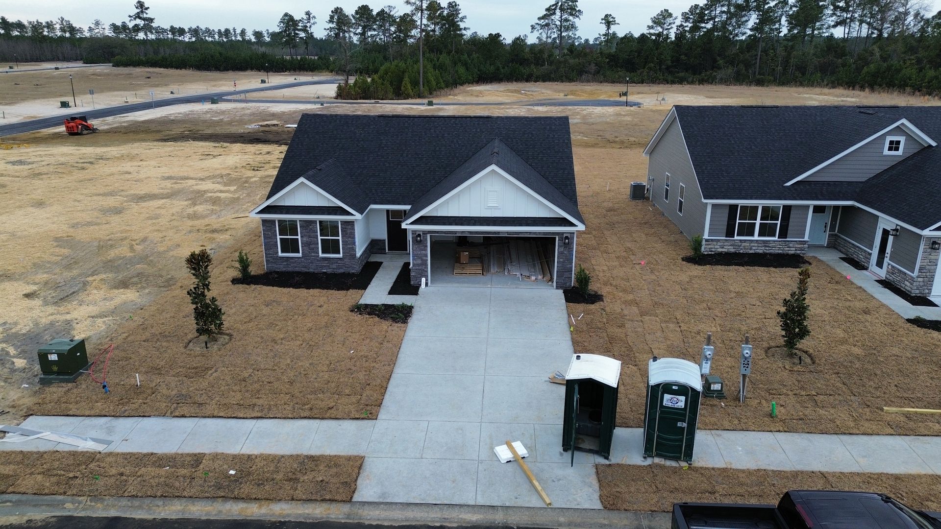 New house under construction with concrete driveway and porta-potties.