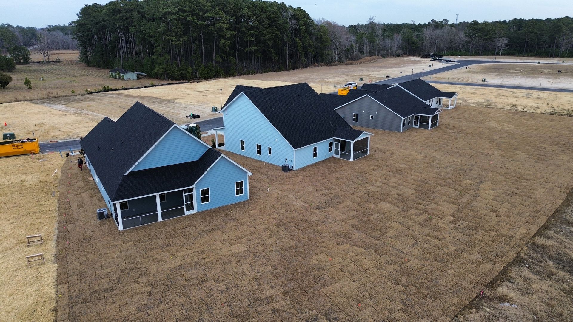 Three newly built houses with dark roofs and light blue/gray siding in a field.